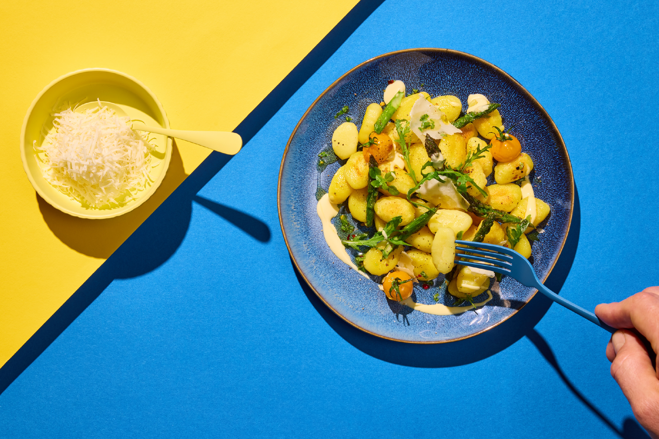 Gnocchi with asparagus, cherry tomatoes, and cheese on a blue plate with a fork.
