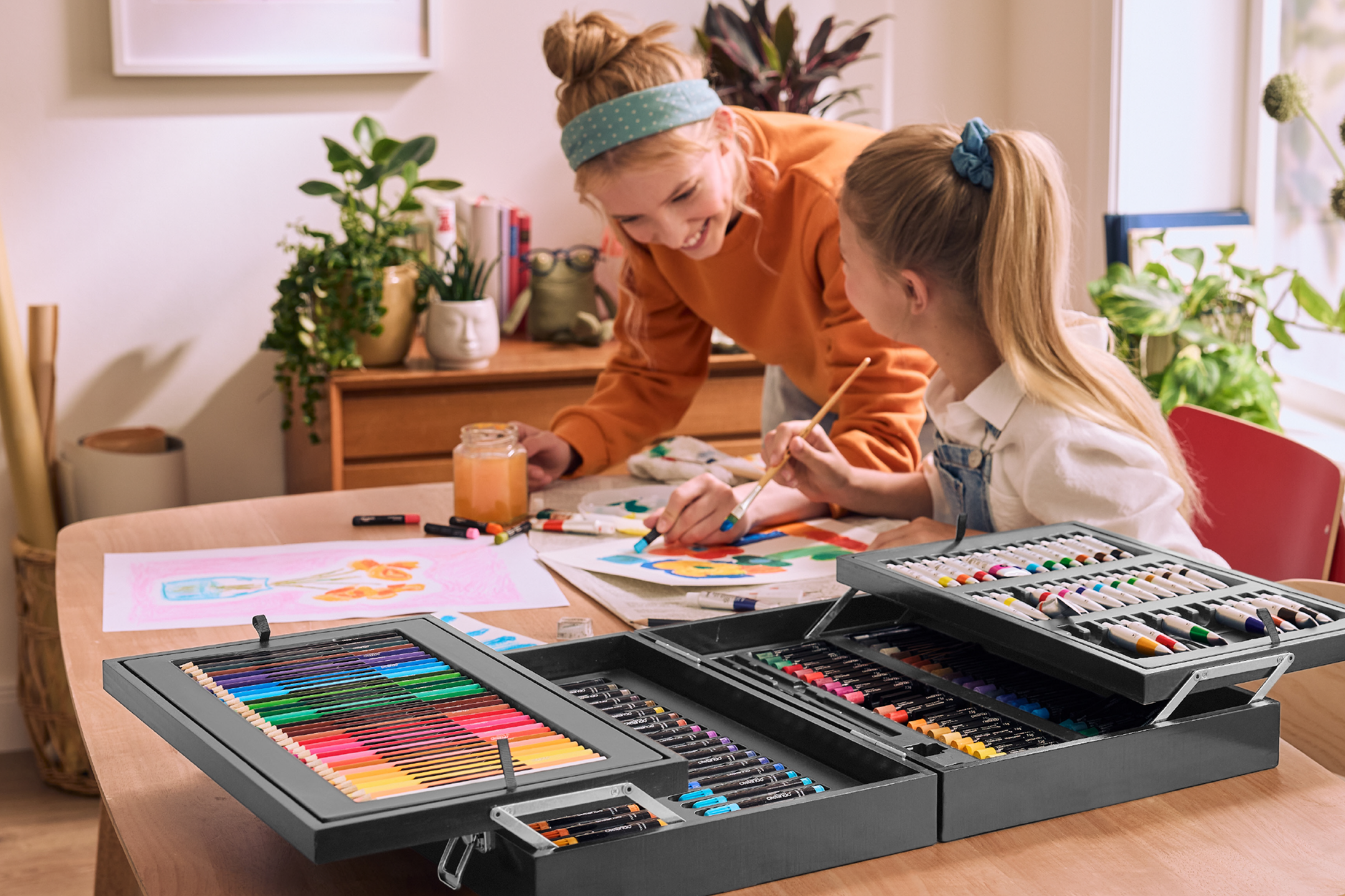 Two girls painting with a large art set, including colored pencils, markers, and paints.