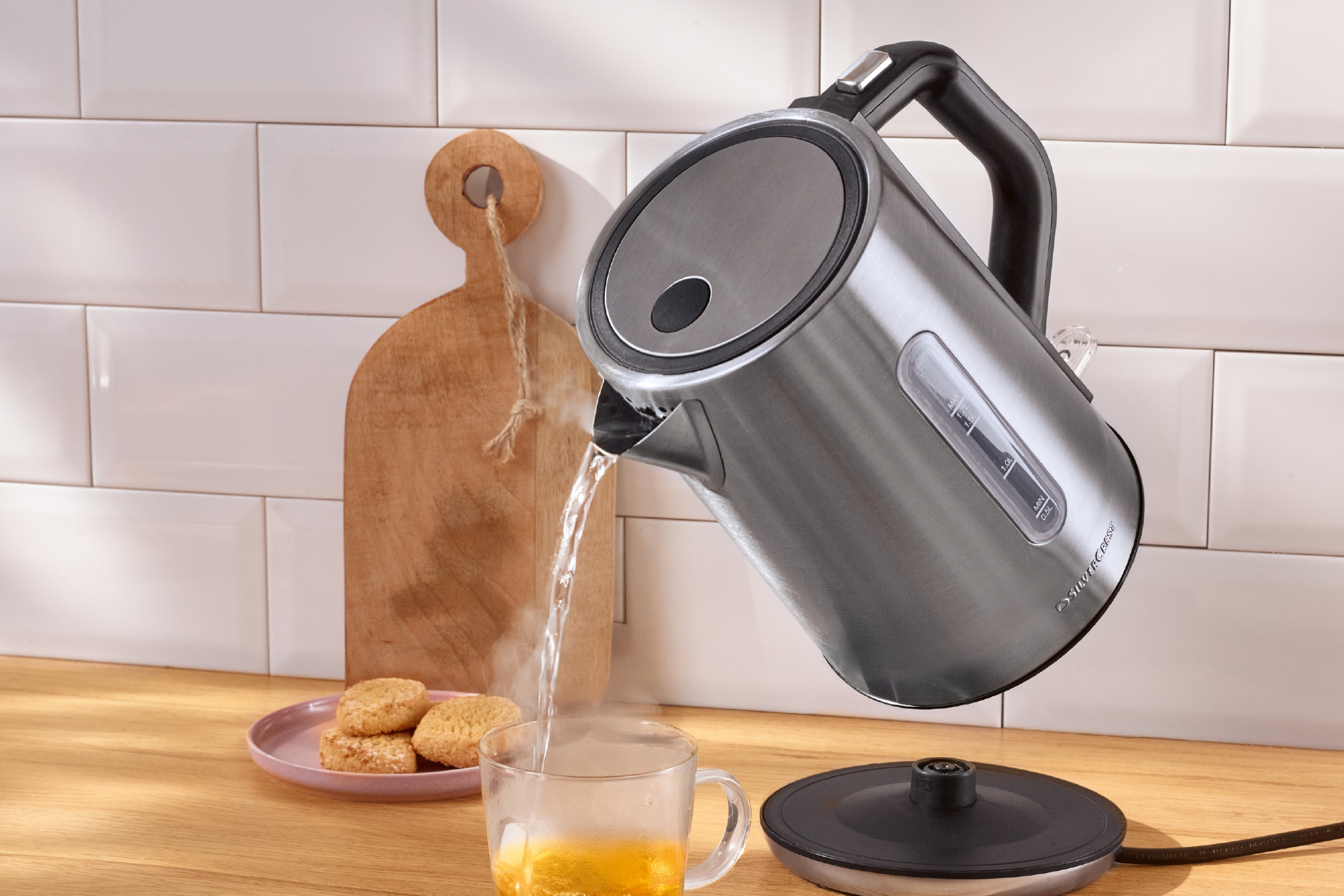 SilverCrest kettle pouring hot water into a mug with cookies on a wooden counter.