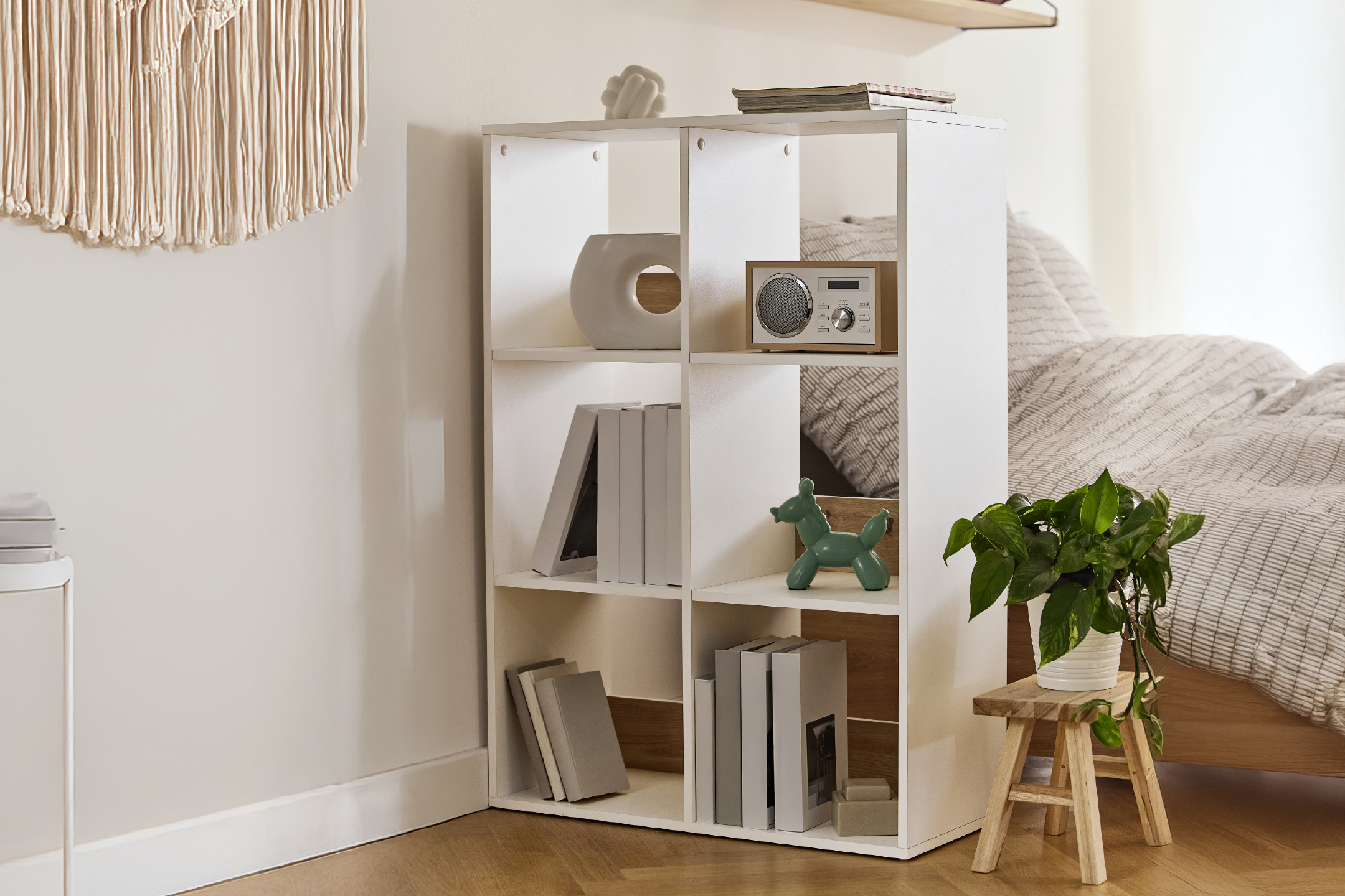 White cube storage unit with books, decor, and a radio, next to a bed and plant