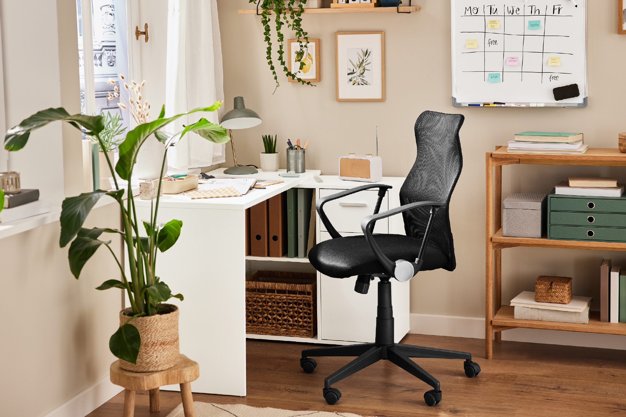 Home office with white desk, black office chair, plants, and a weekly planner.