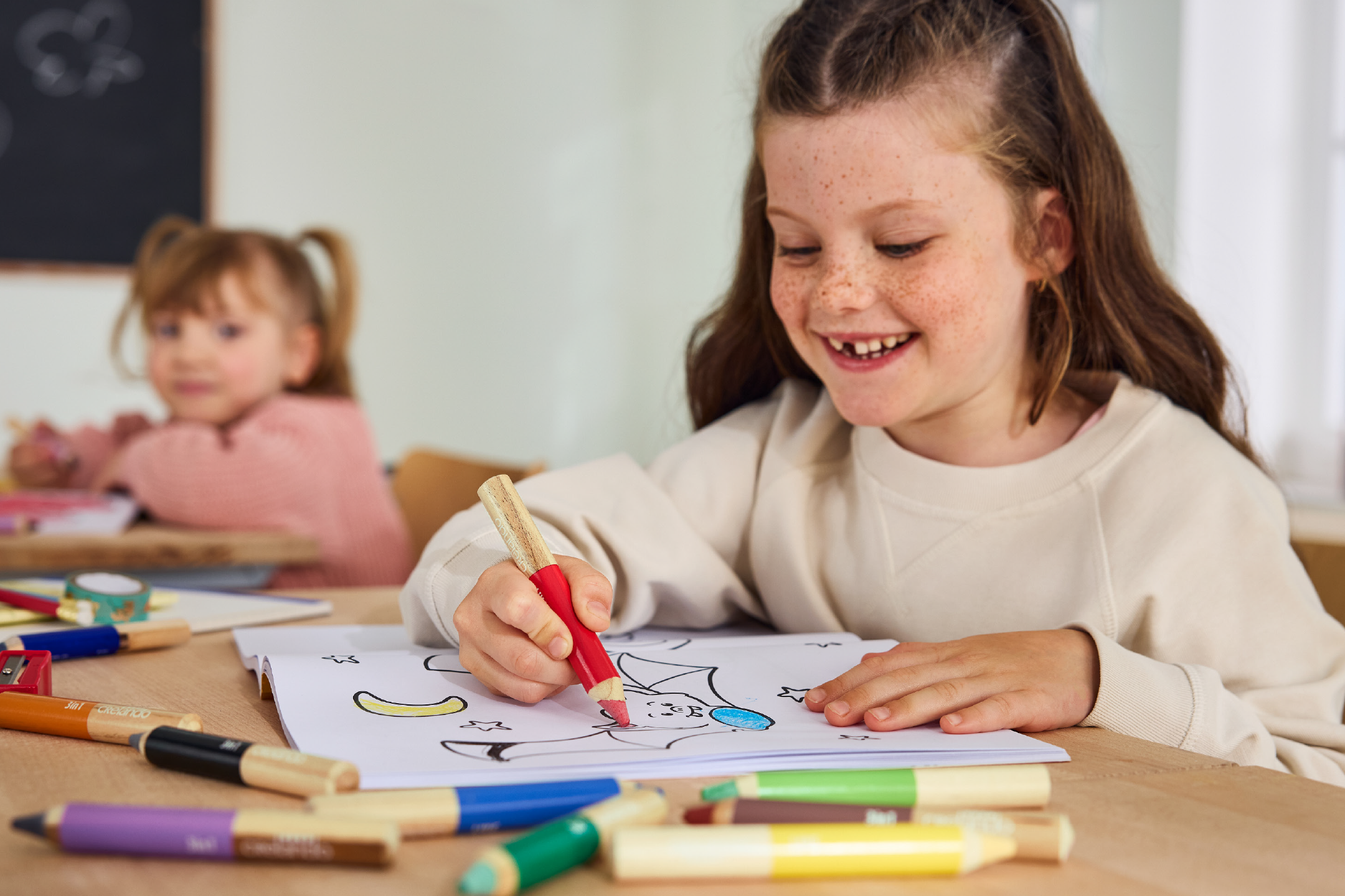 Smiling girl coloring with Crelando pencils, another child in the background.