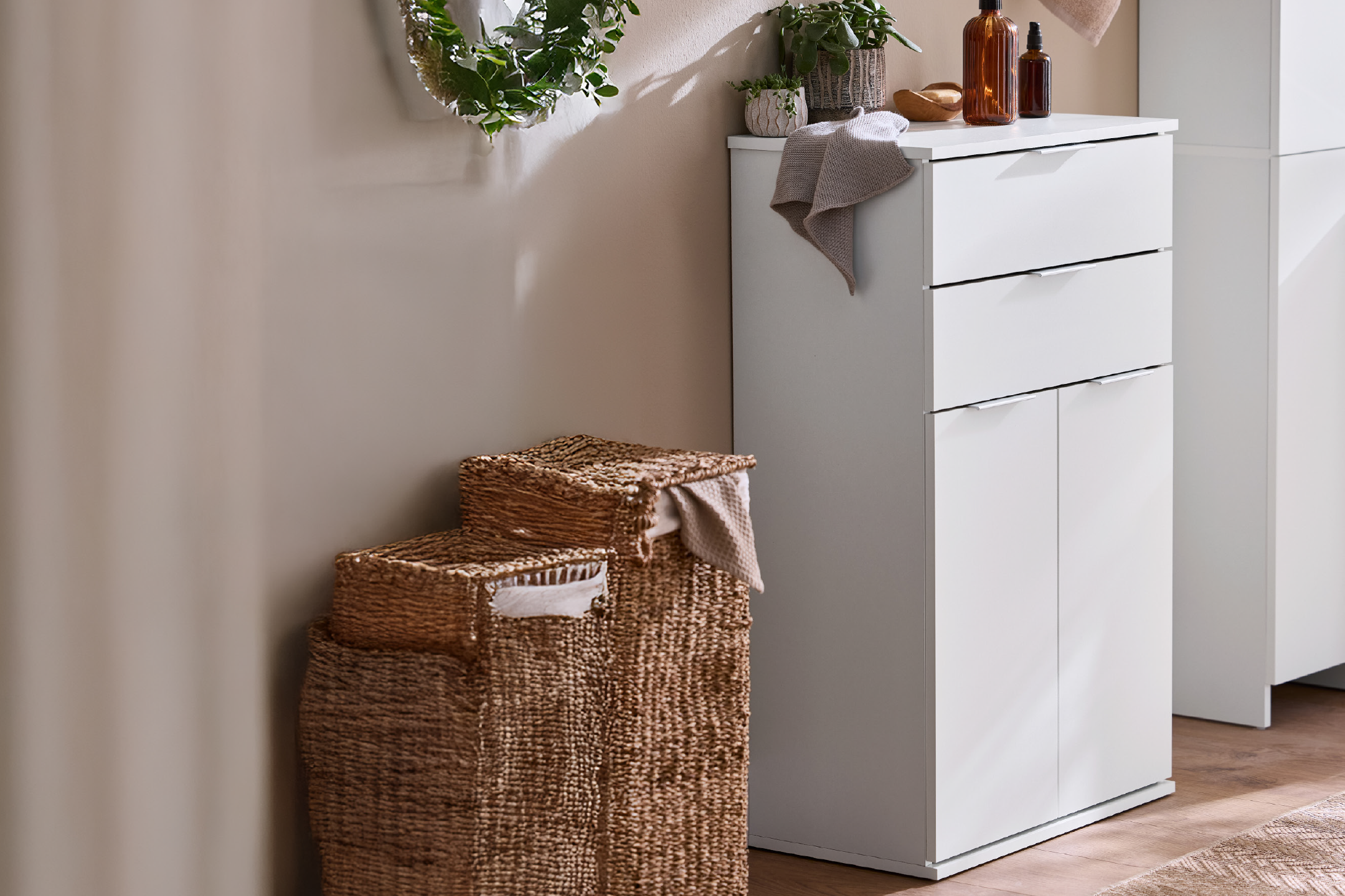 White bathroom cabinet with drawers and doors, next to woven laundry baskets.