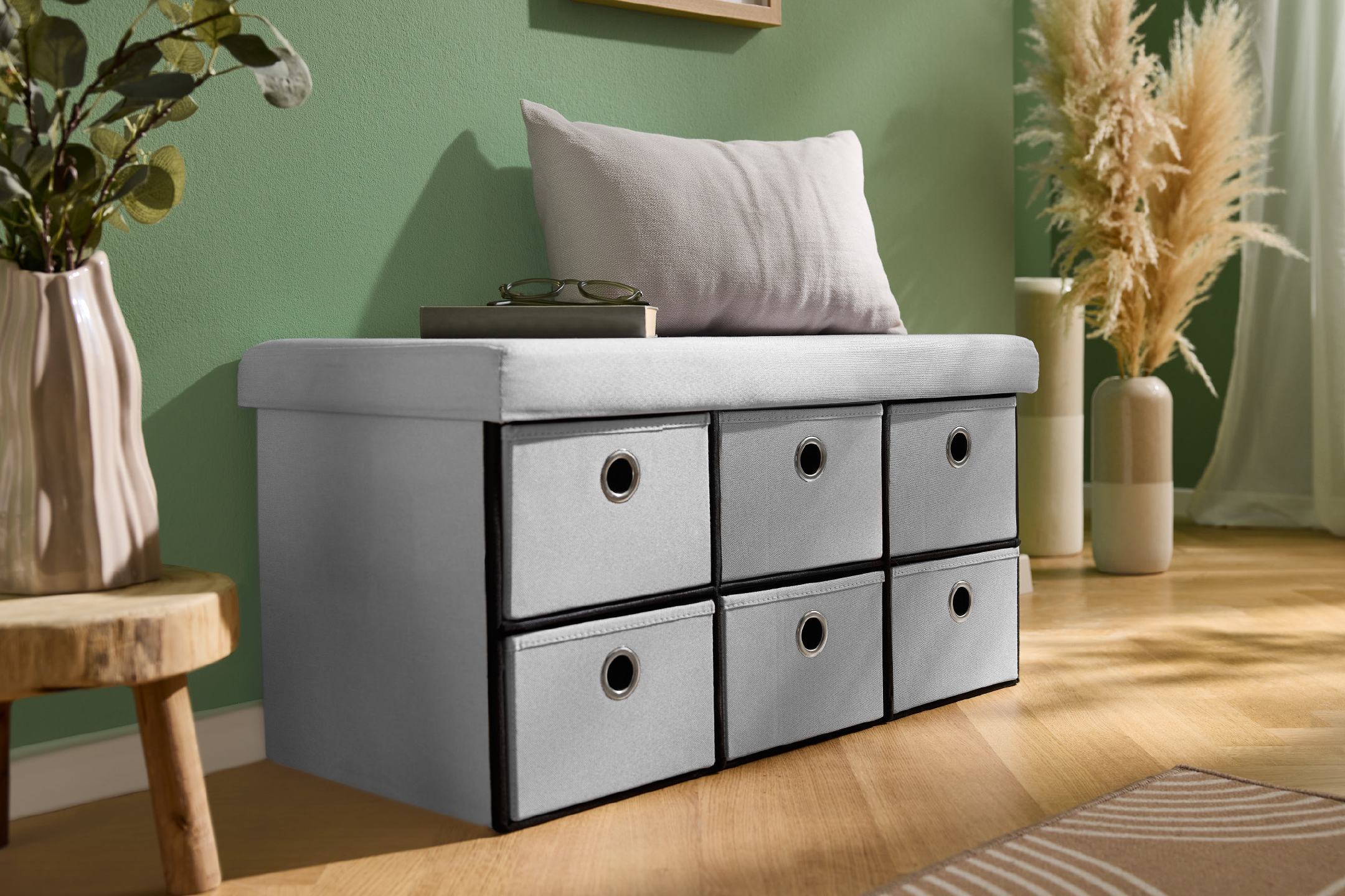 Γκρι πάγκος αποθήκευσης με έξι υφασμάτινα συρτάρια, ένα μαξιλάρι και διακοσμητικά φυτά σε σαλόνι.
