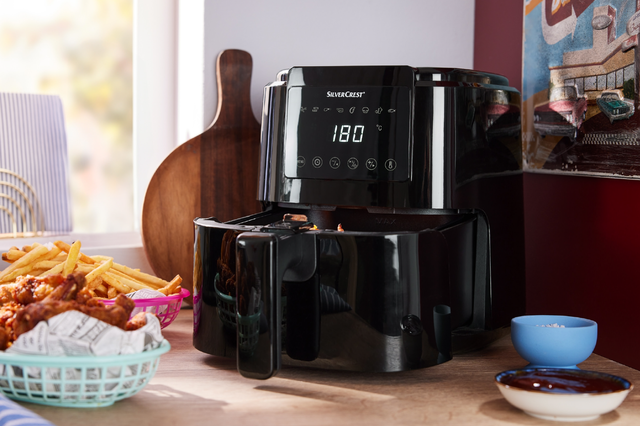 Μαύρη φριτέζα αέρος σε ξύλινο πάγκο με πατάτες και κοτόπουλο σε καλάθια, και σάλτσες.