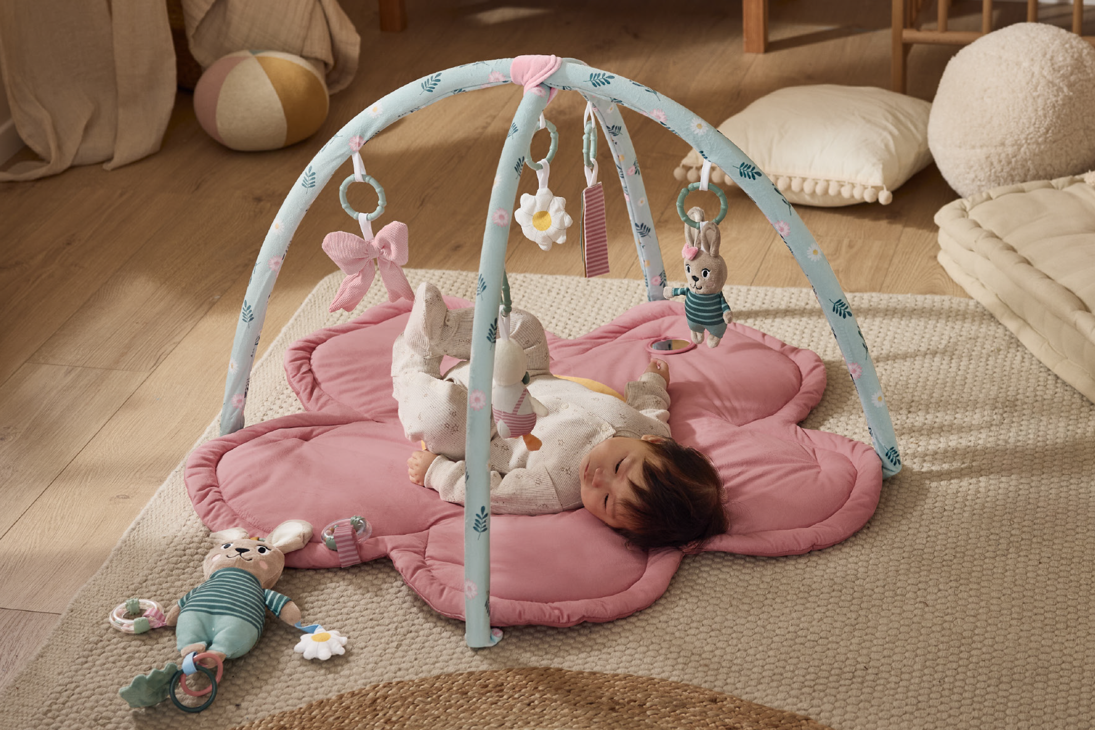 Μωρό ξαπλωμένο σε ροζ χαλάκι παιχνιδιού σε σχήμα λουλουδιού με αψίδα δραστηριοτήτων και κρεμαστά παιχνίδια.
