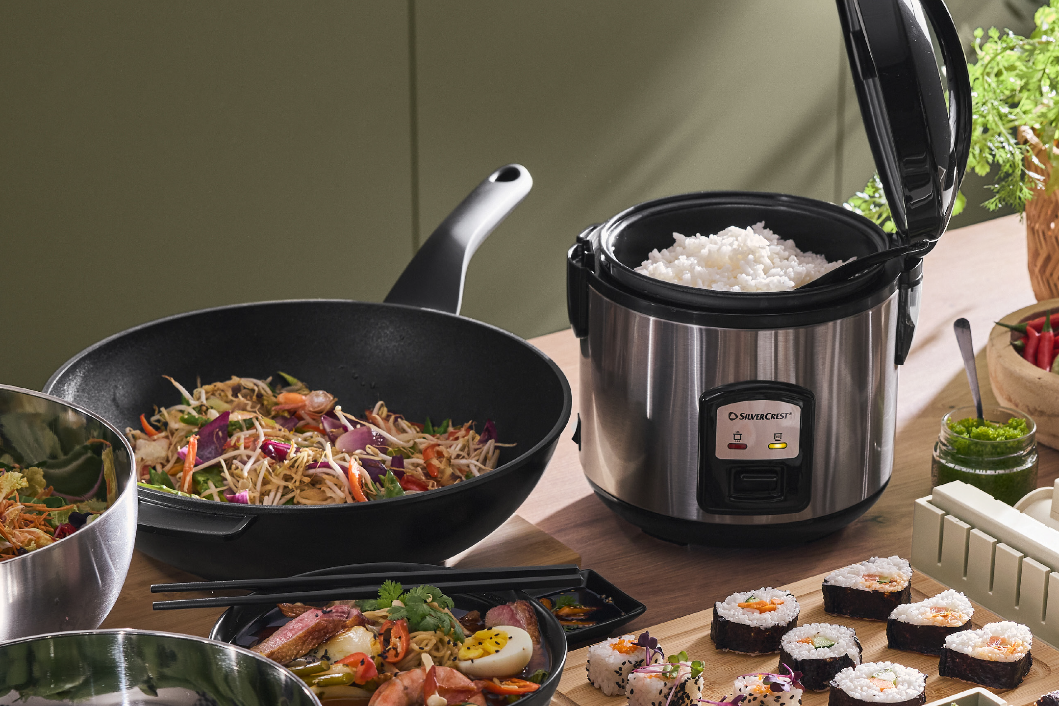 Ρυζομάγειρας με μαγειρεμένο ρύζι, γουόκ με stir-fry, σούσι και ασιατικά πιάτα σε ξύλινο τραπέζι.