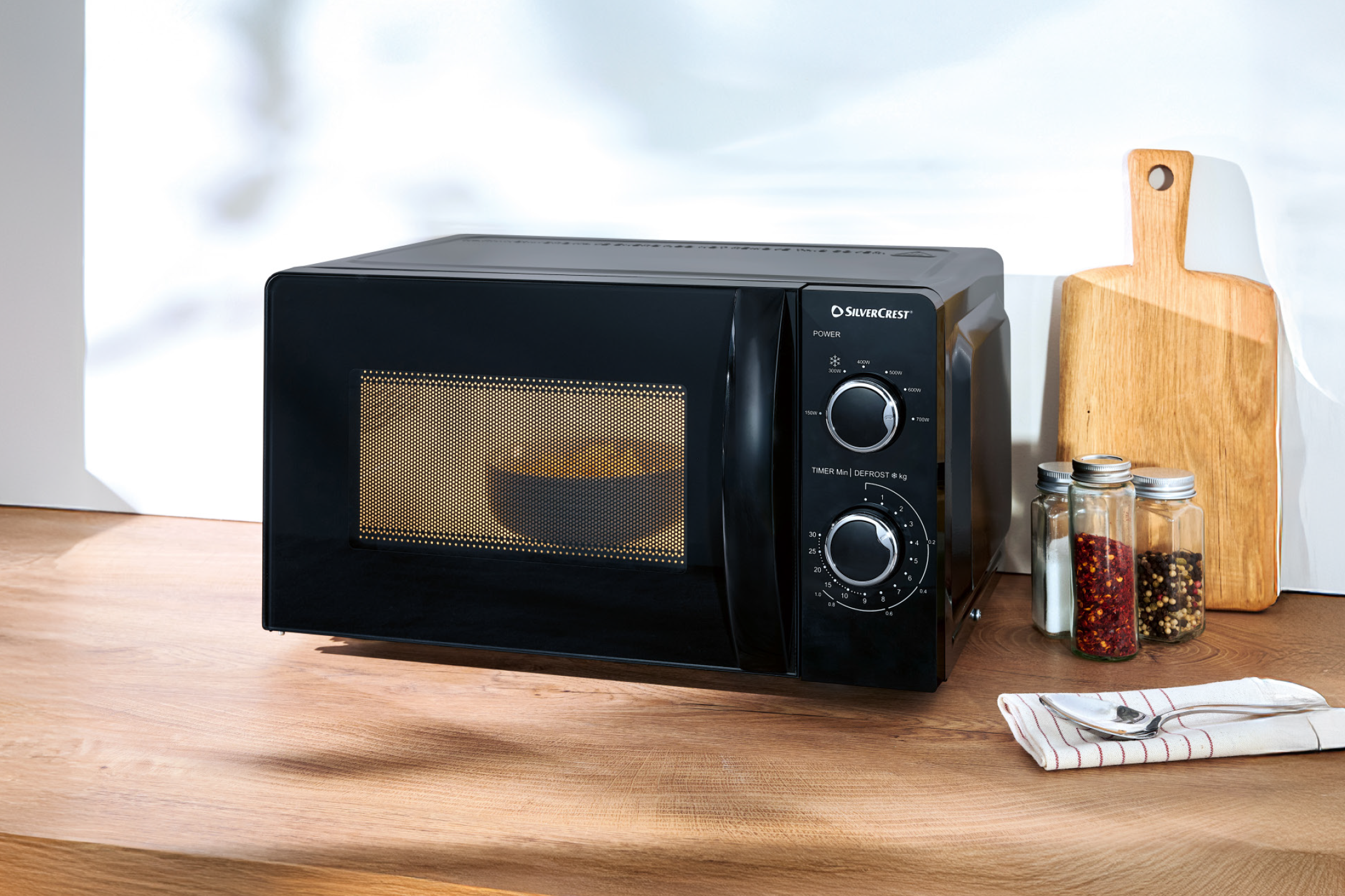 Black microwave oven on a wooden counter with spices and a cutting board.