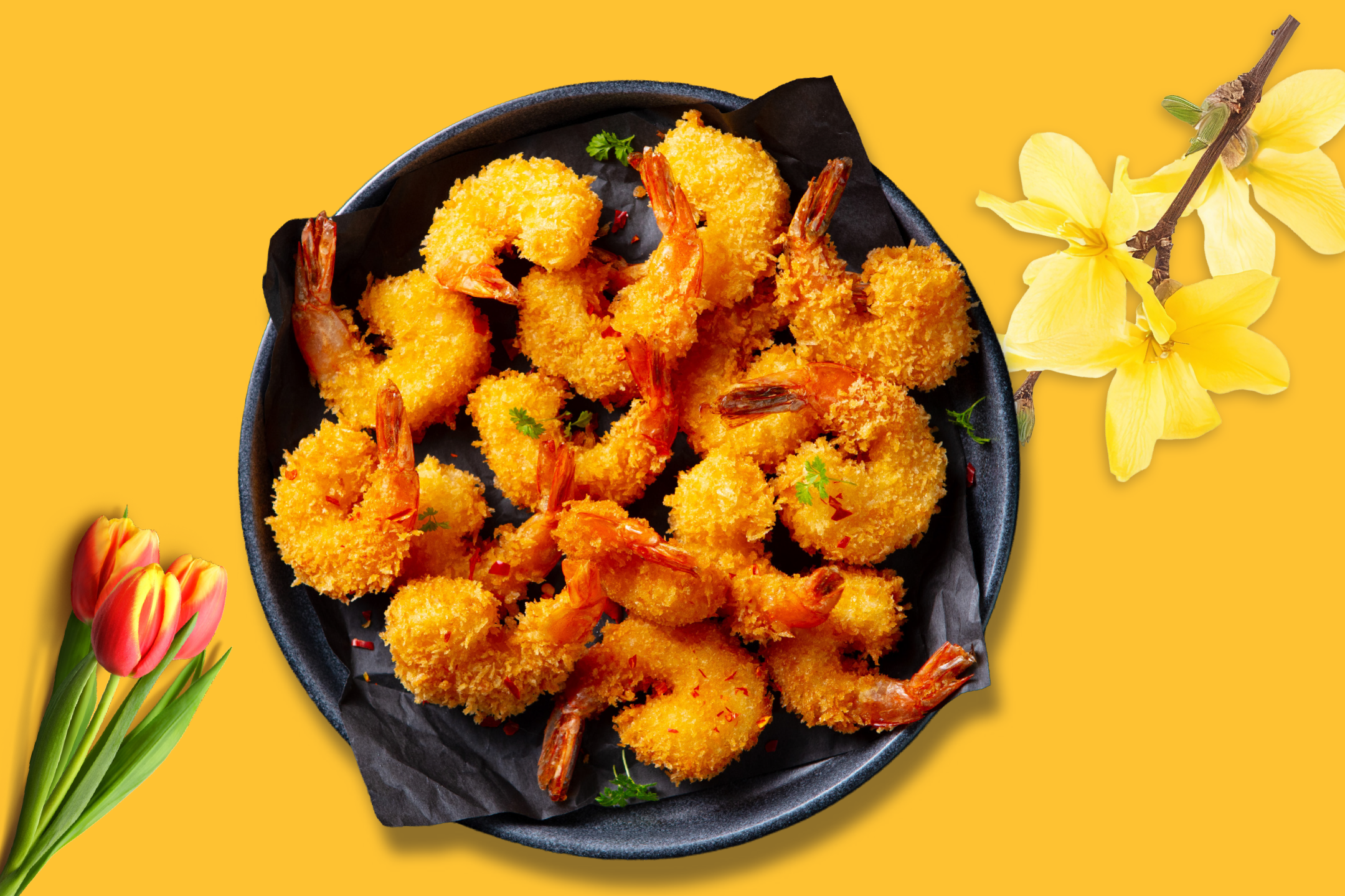 Crispy fried shrimp on a black plate, with tulips and yellow flowers on a yellow background.