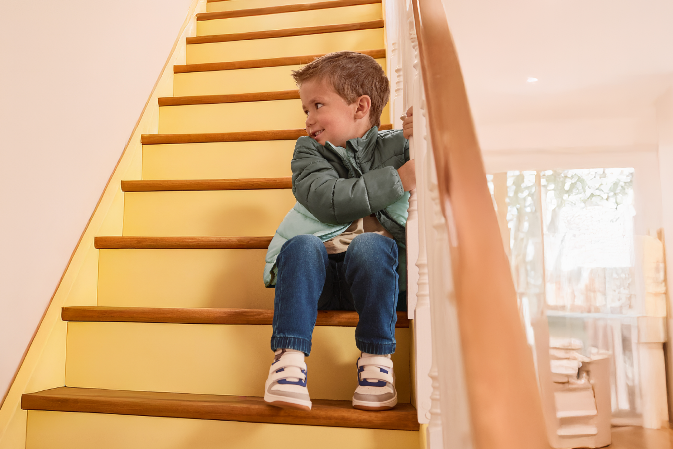 Smiling boy in a puffer jacket and jeans sitting on wooden stairs.
