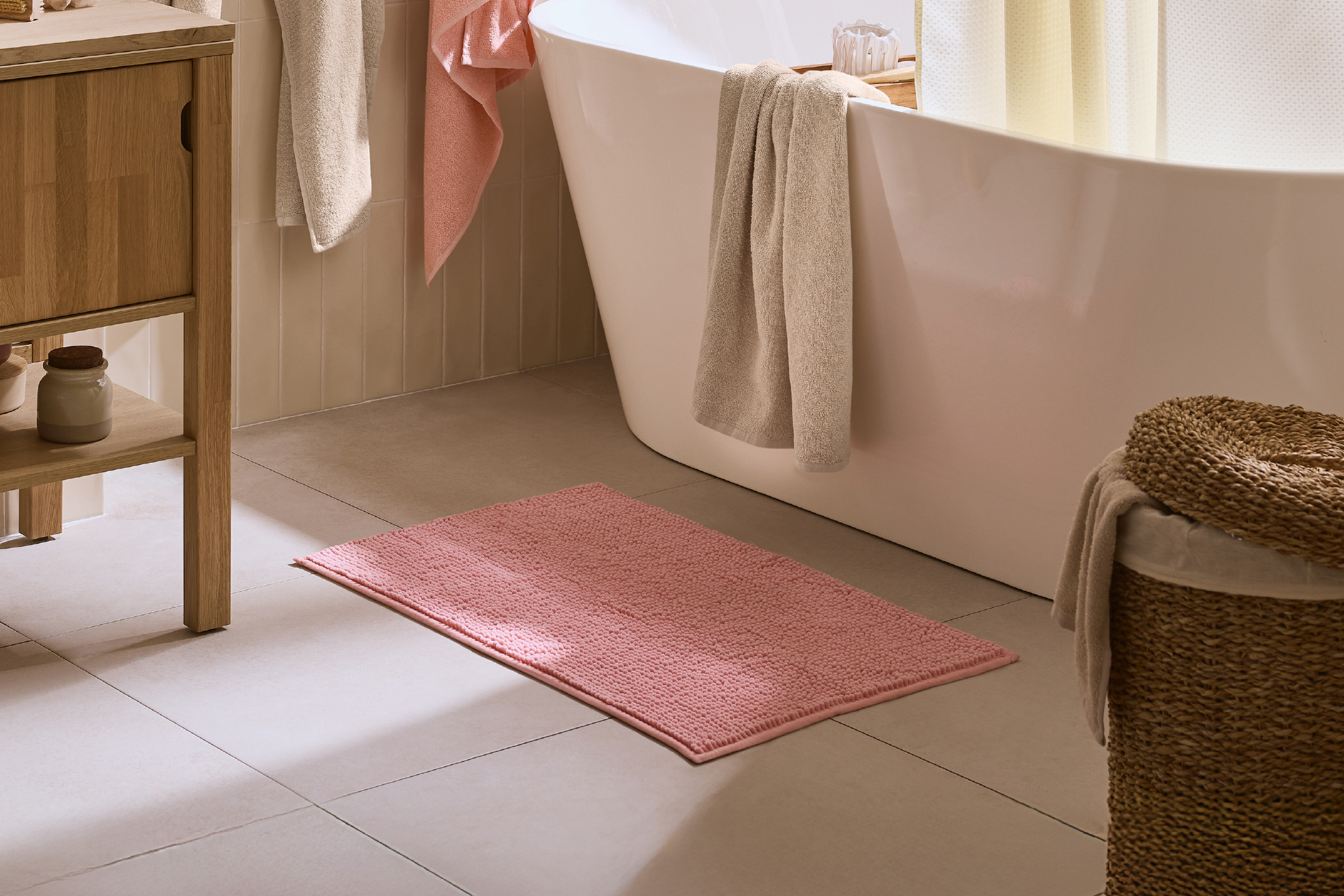 Bathroom with a pink bath mat, white bathtub, and wooden cabinet.