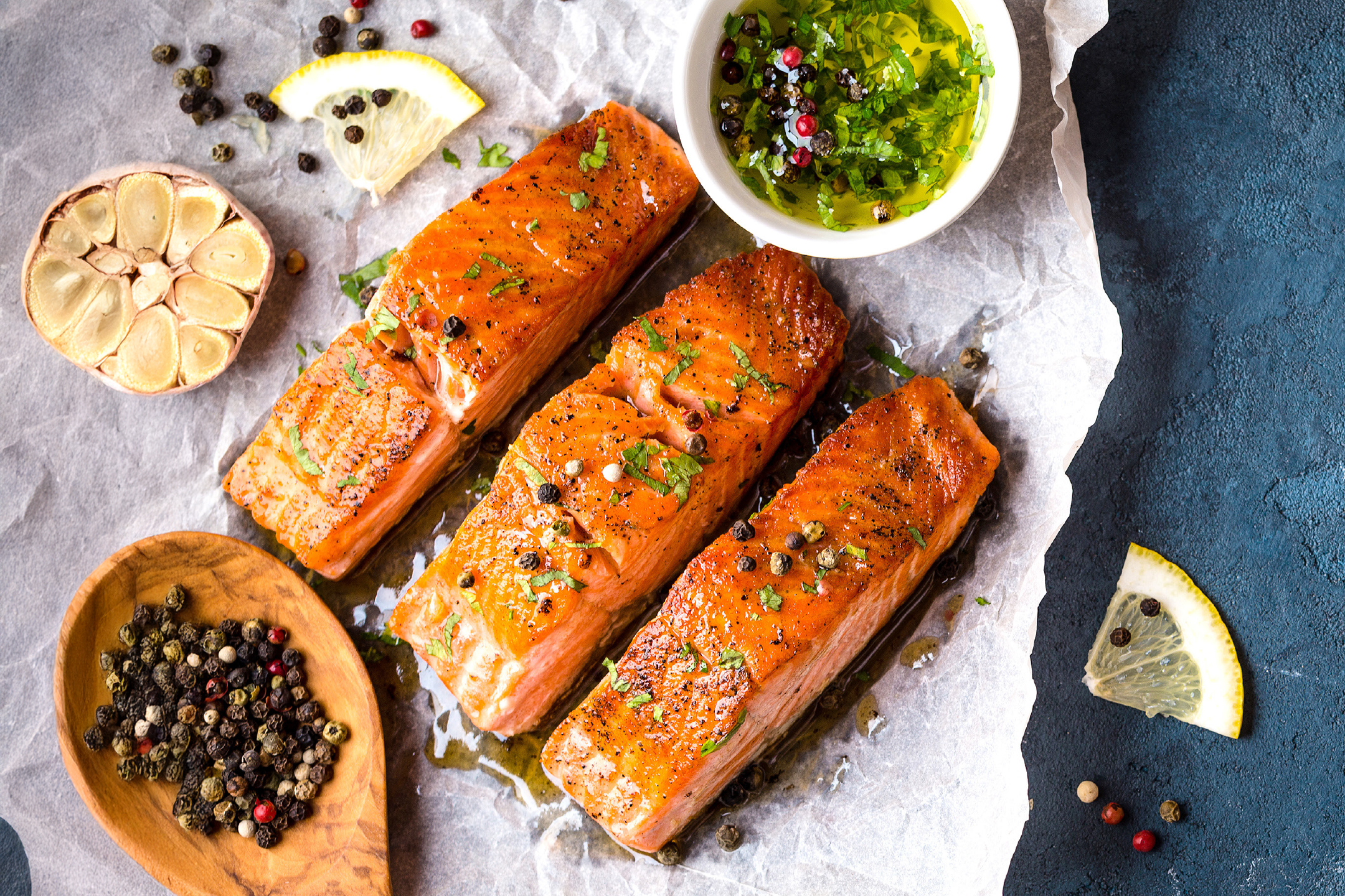 Τρία μαγειρεμένα φιλέτα σολομού με μυρωδικά, λεμόνι, σκόρδο και πιπέρια σε λαδόκολλα.