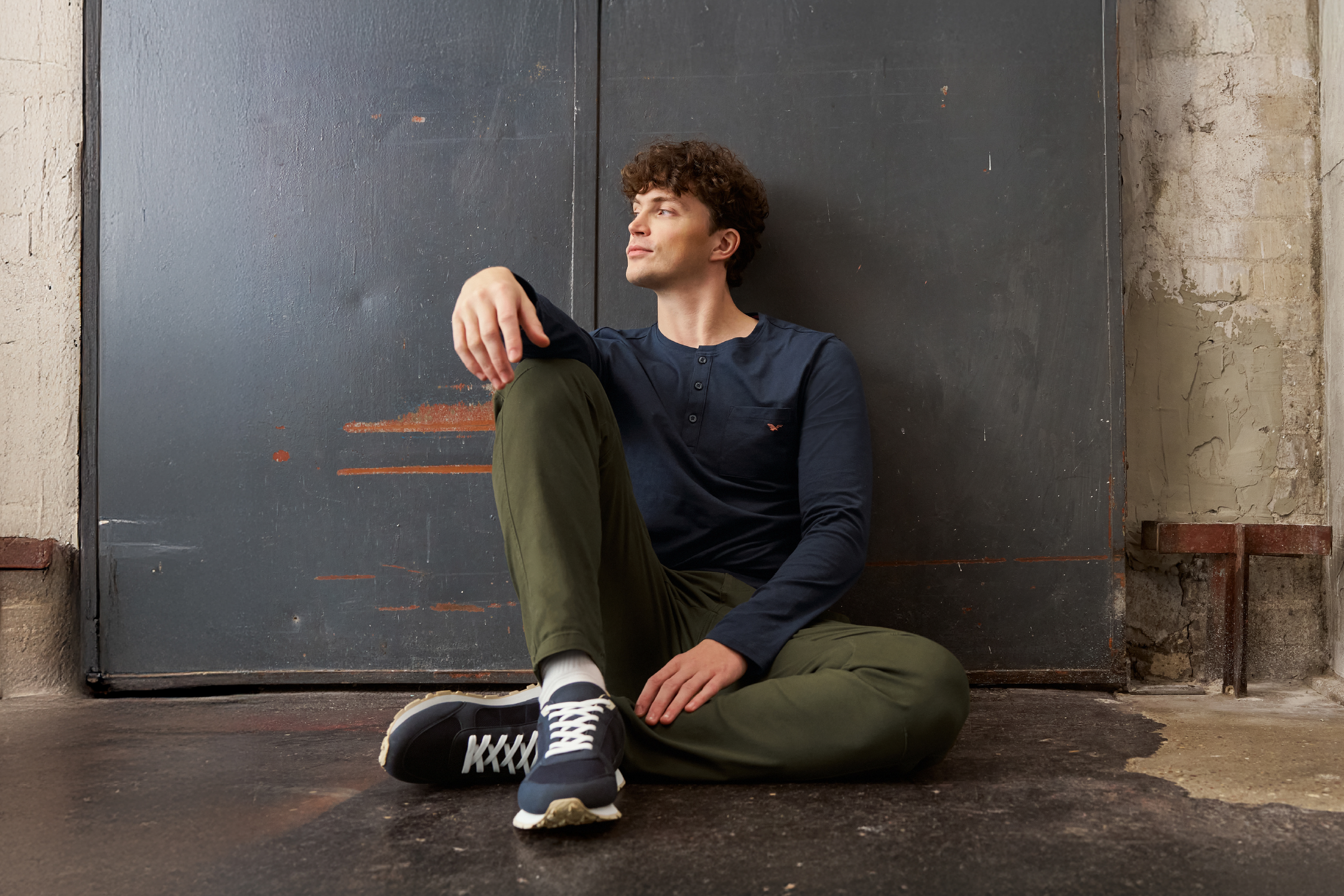 Άνδρας με μακρυμάνικο μπλουζάκι Henley σε ναυτικό μπλε και χακί φόρμα, κάθεται στο πάτωμα.