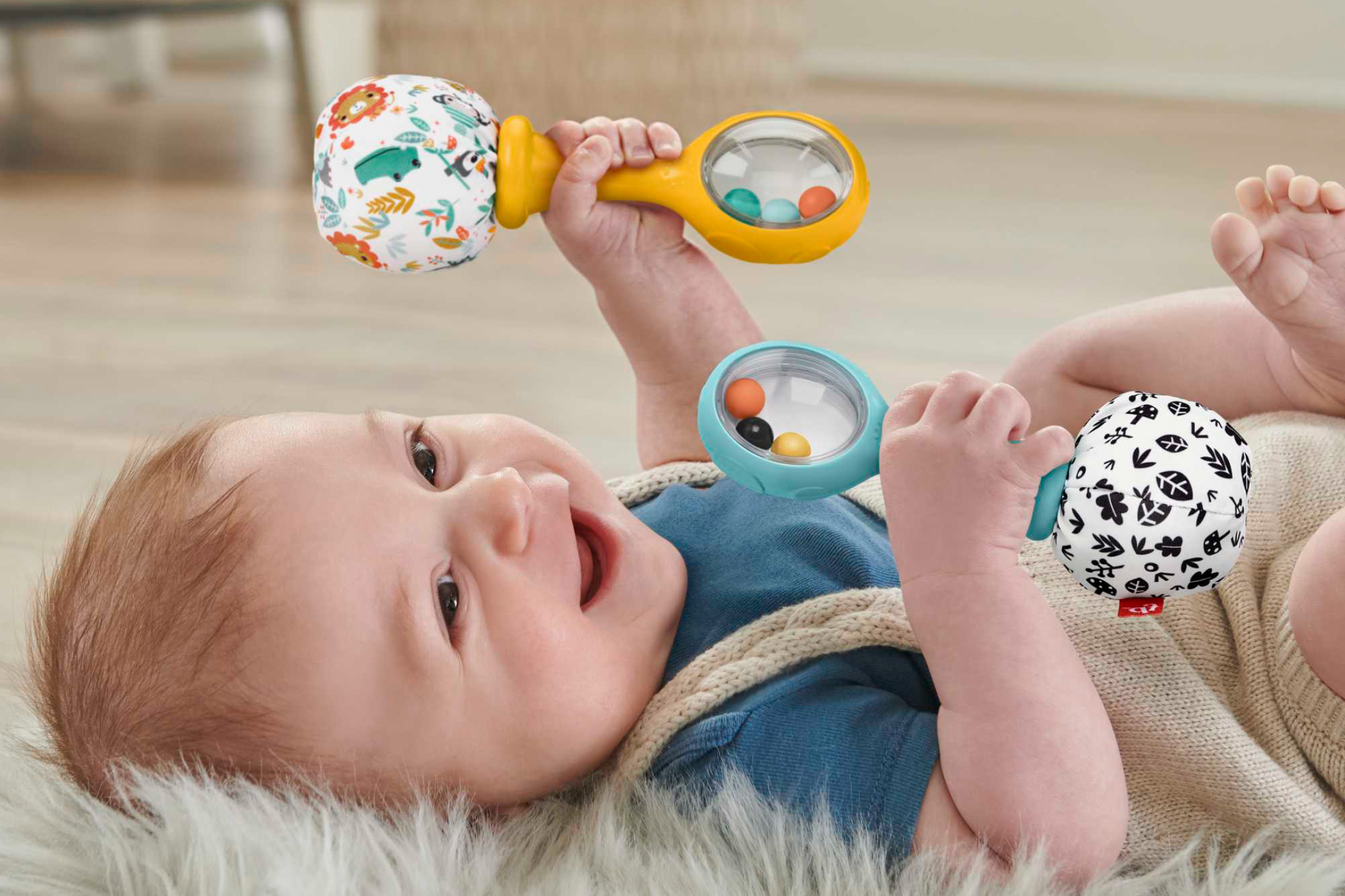 Happy baby playing with two colorful dumbbell-shaped rattles on a fluffy rug.
