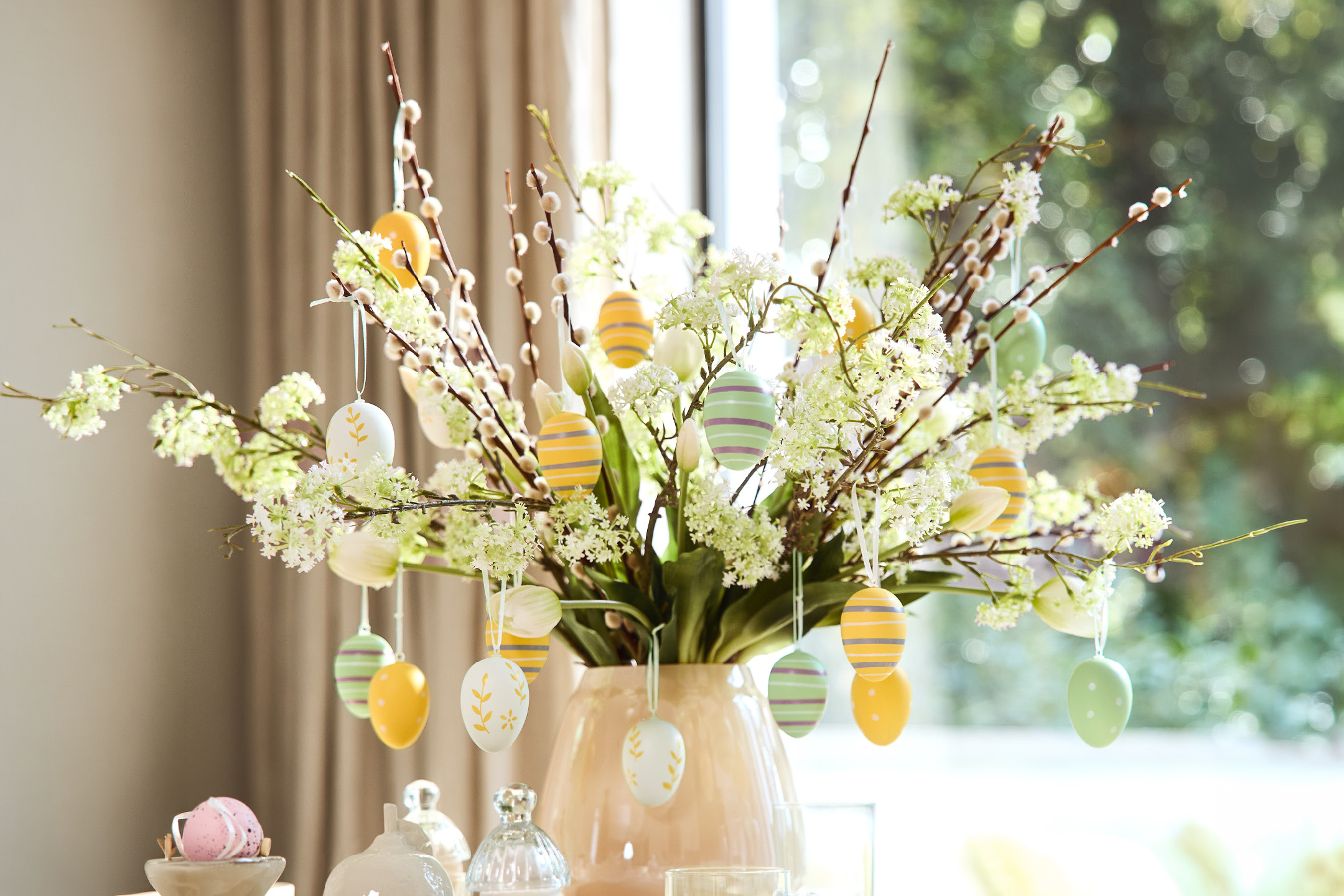 Πασχαλινή διακόσμηση με κλαδιά ιτιάς, λευκά λουλούδια και πολύχρωμα κρεμαστά αυγά.