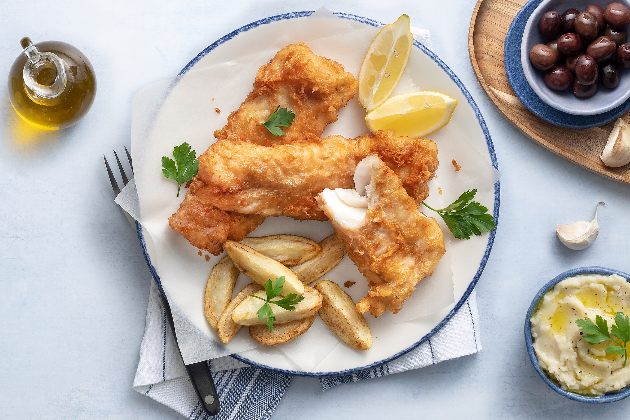 Τραγανό τηγανητό ψάρι με πατάτες wedges, λεμόνι, ελιές και πουρέ πατάτας.