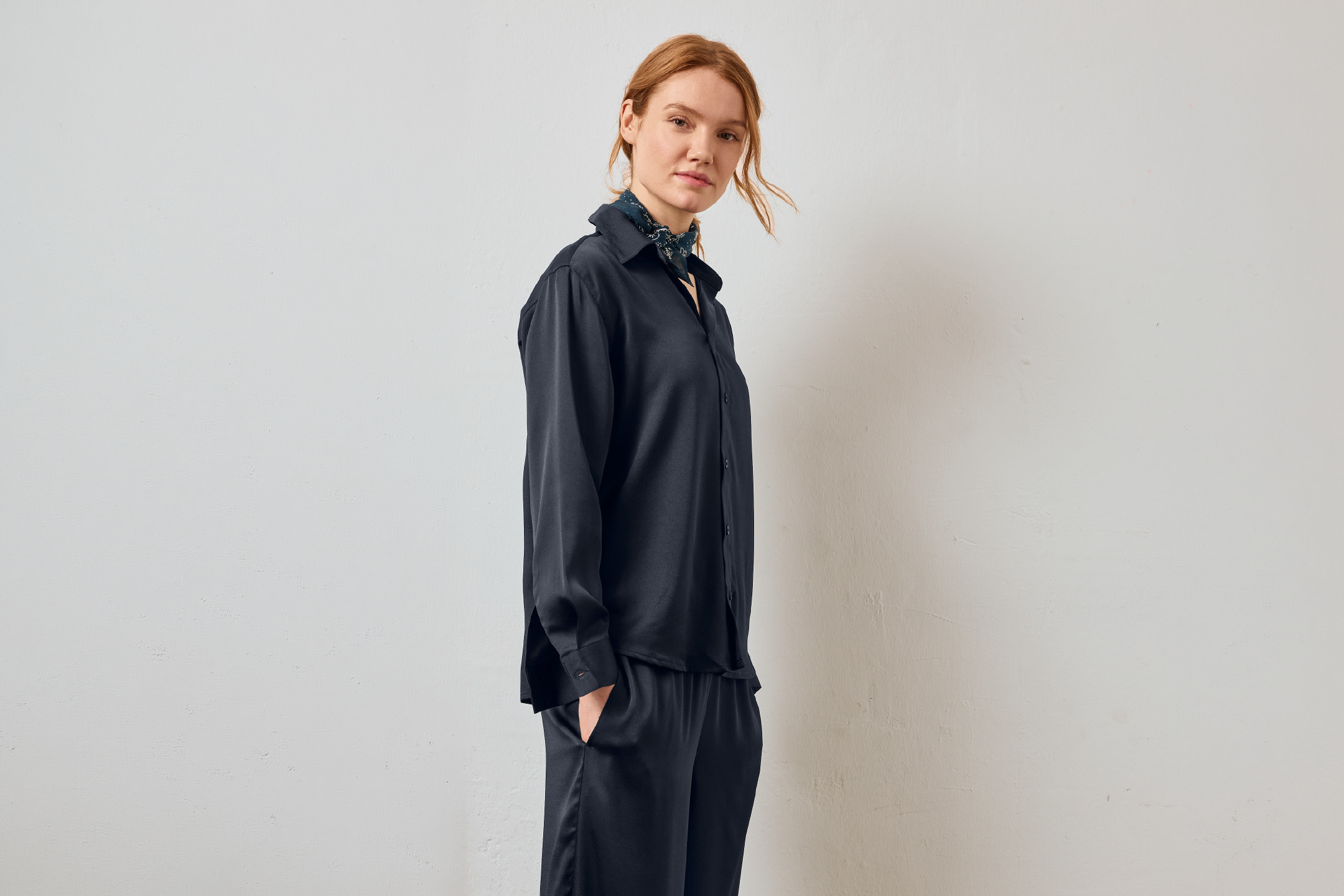 Γυναίκα με μαύρο σατέν πουκάμισο και παντελόνι με ένα φουλάρι με σχέδια.