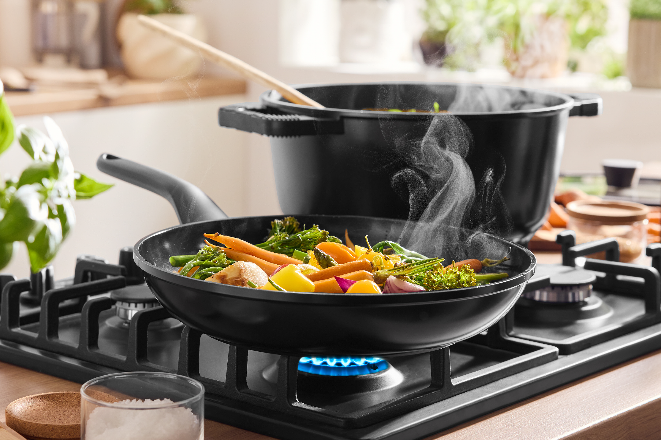 Steaming vegetables cooking in a pan and pot on a gas hob in a kitchen.