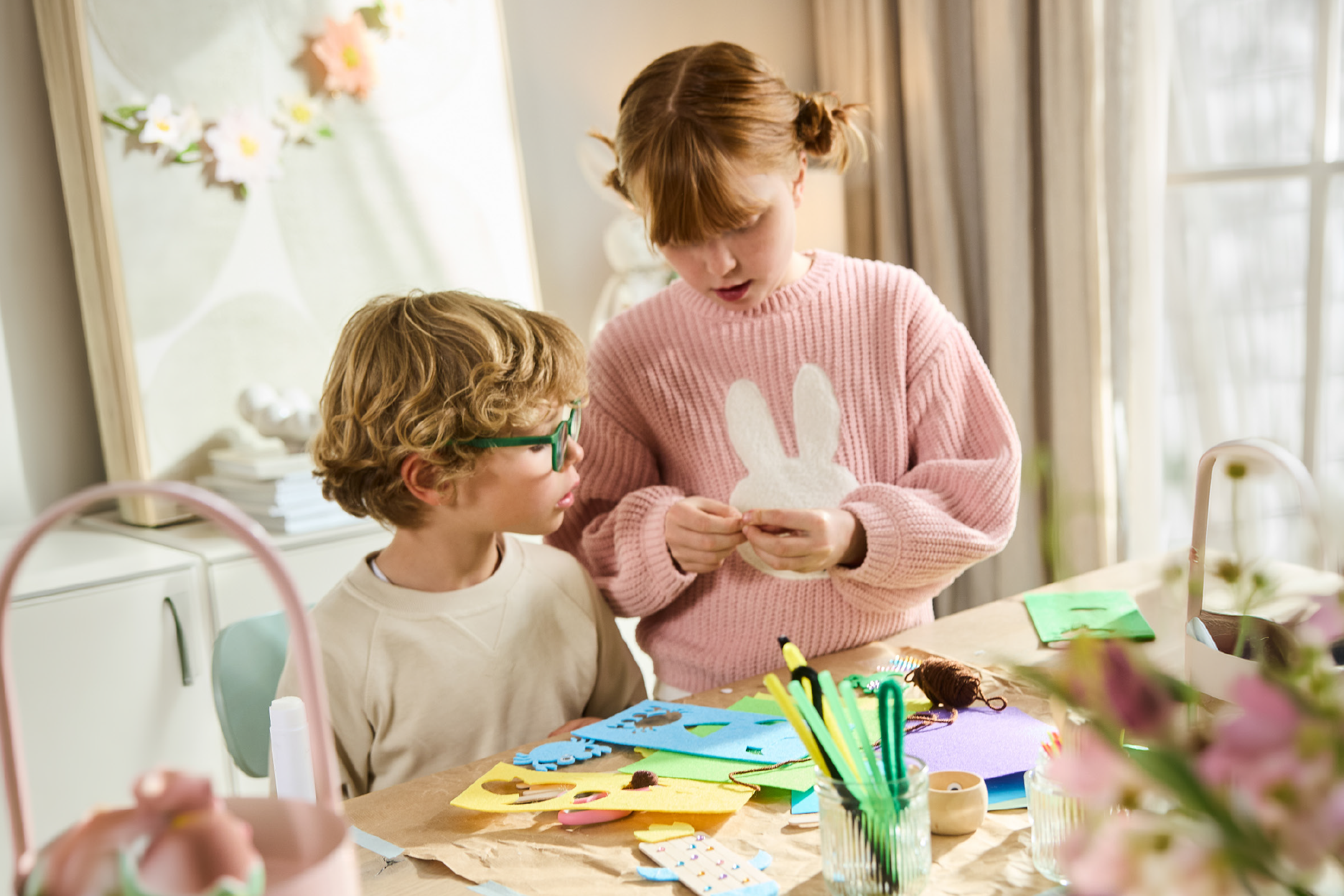 Two children crafting Easter decorations with felt, yarn, and colorful pens.
