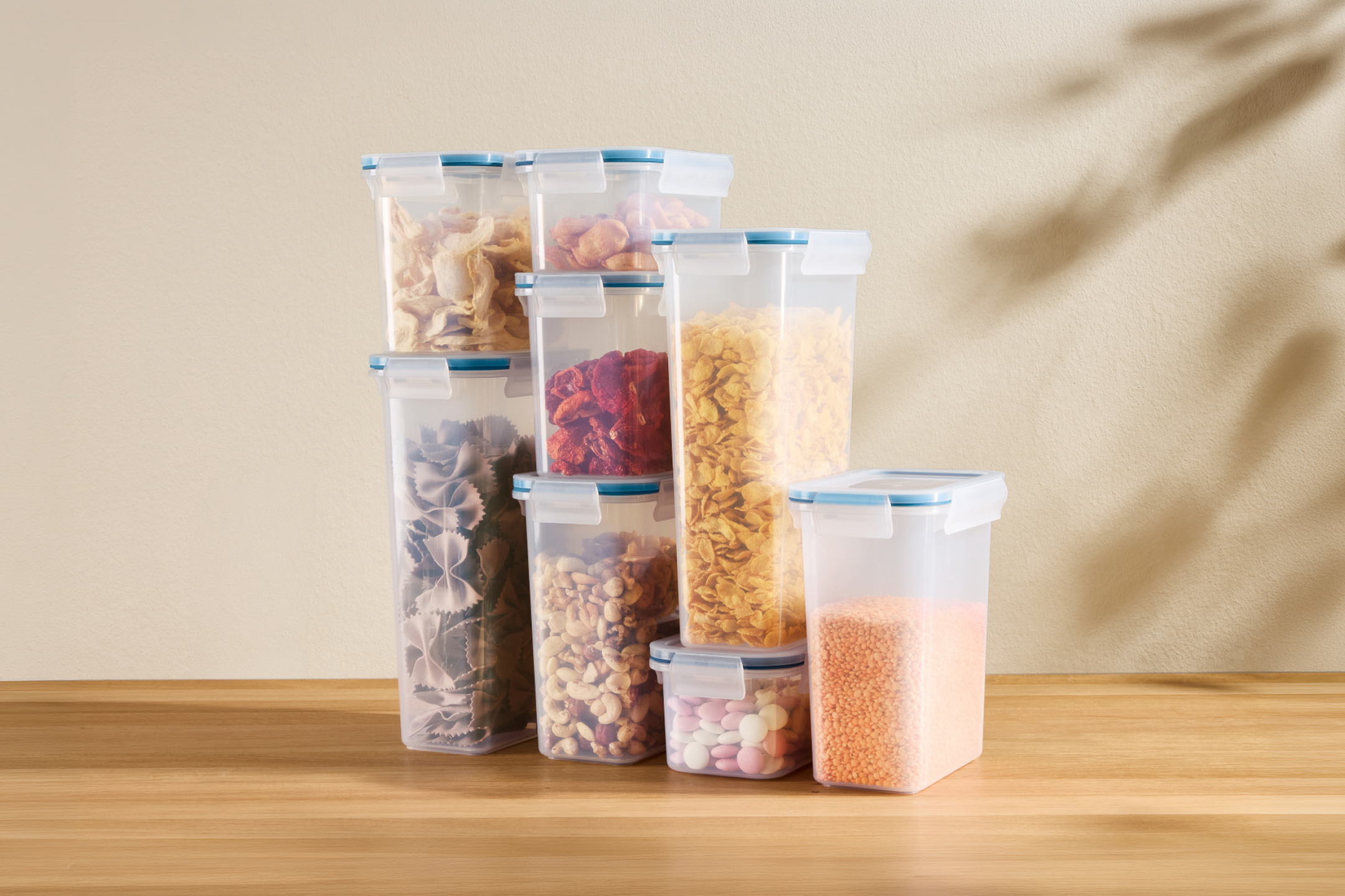 Διαφανή δοχεία αποθήκευσης τροφίμων γεμάτα με ζυμαρικά, ξηρούς καρπούς, φακές, δημητριακά και αποξηραμένα φρούτα.