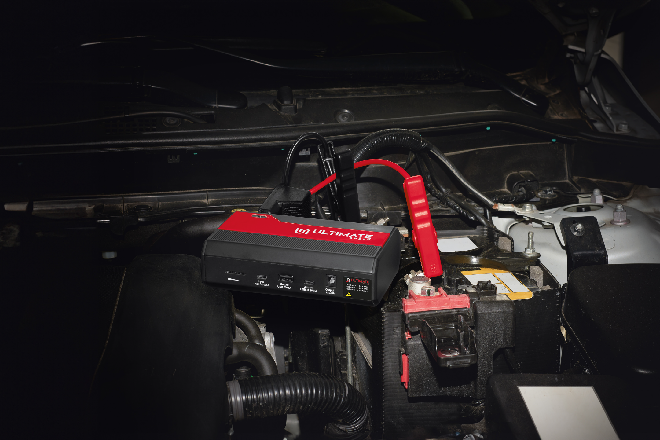 A portable jump starter connected to a car battery in an engine bay.