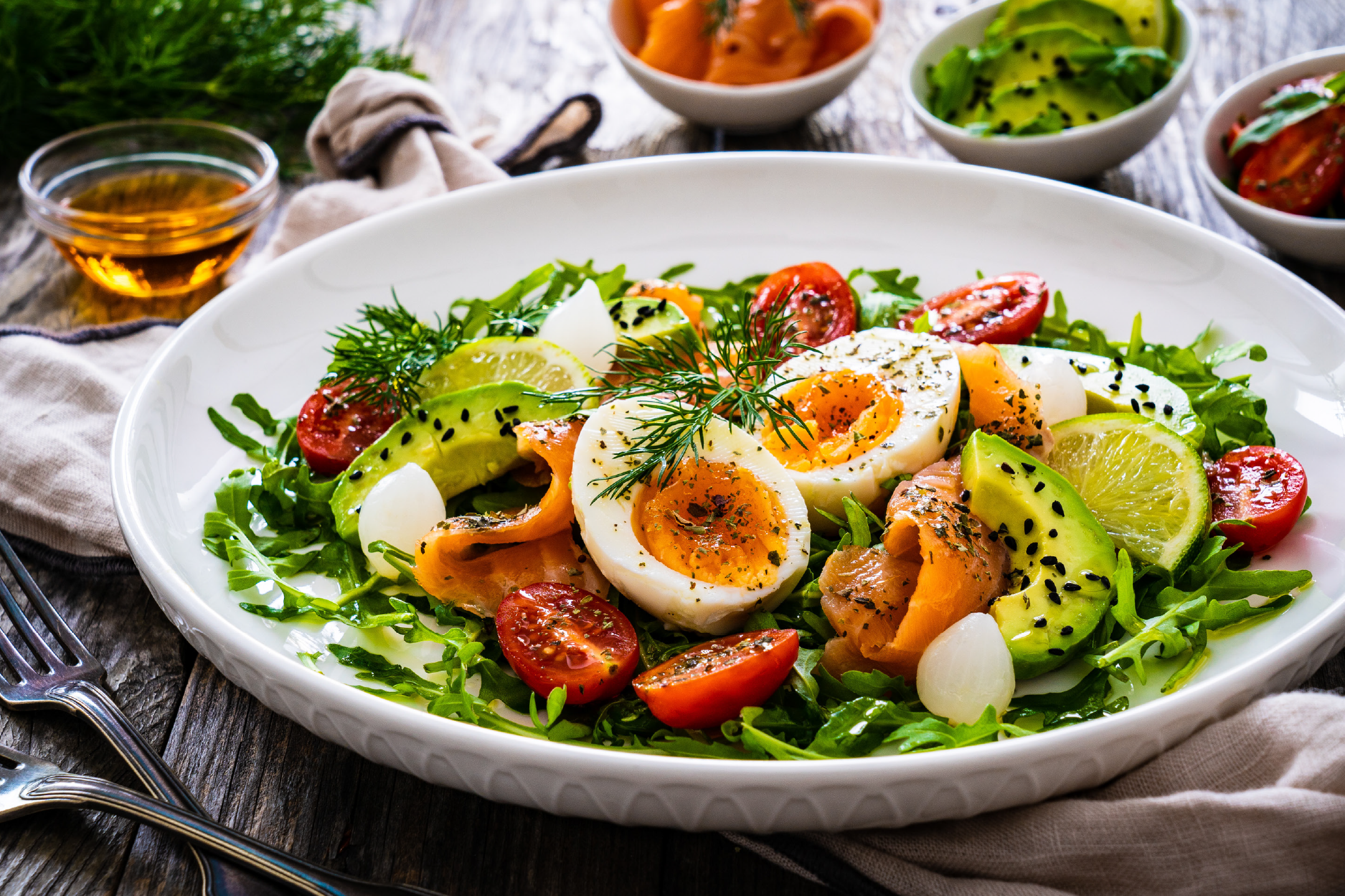 Salmon and egg salad with avocado, cherry tomatoes, and rocket on a white plate.