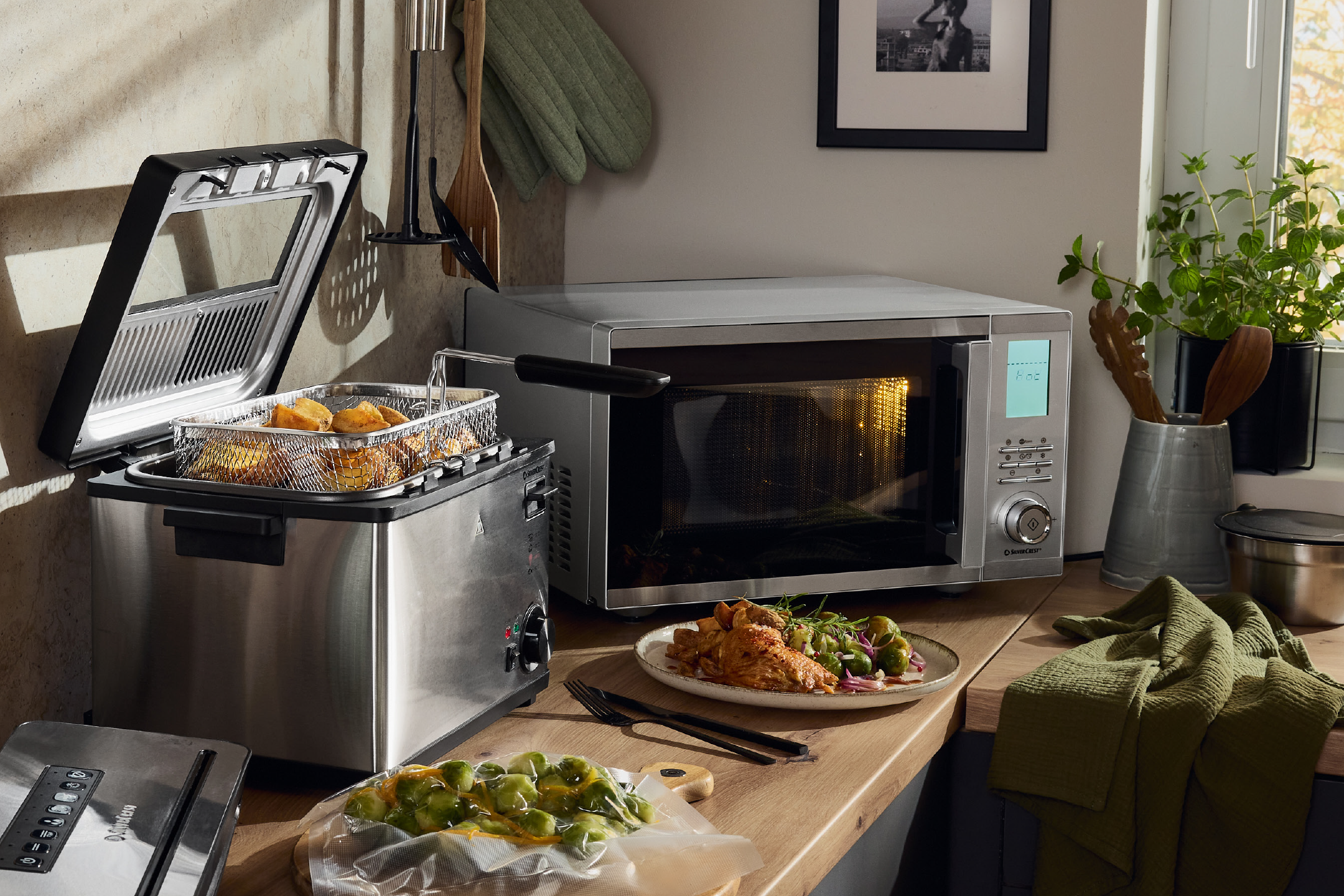 Kitchen scene with a deep fryer, microwave, and a meal of chicken and vegetables.