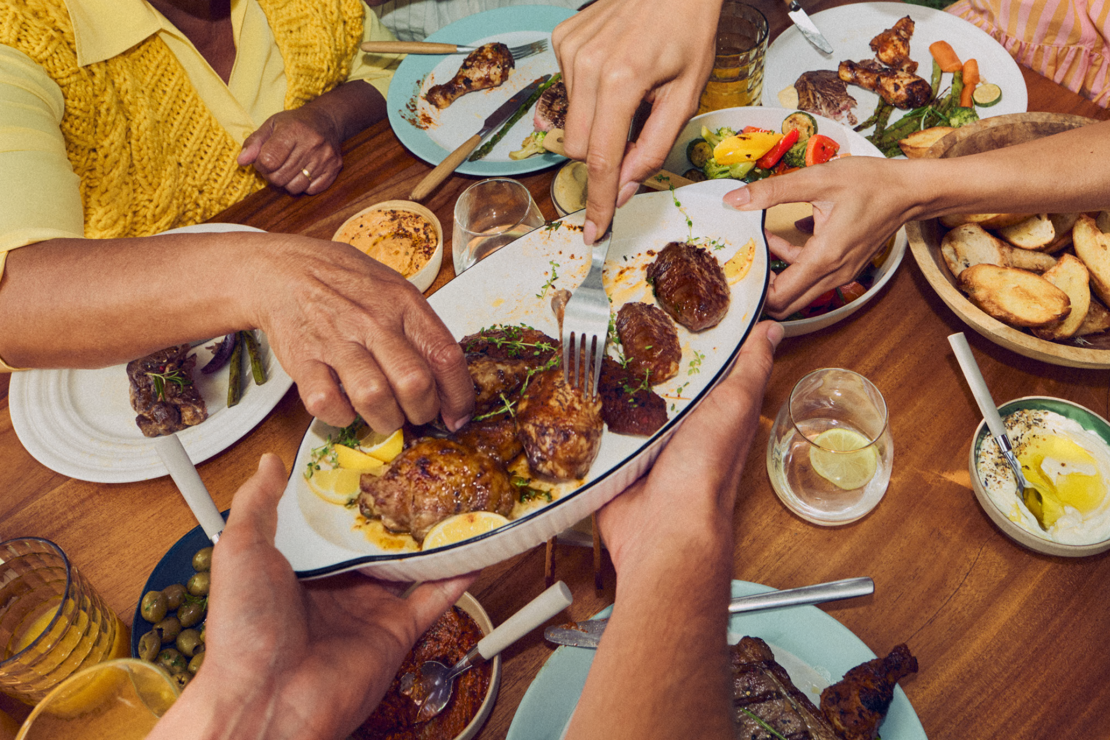Άνθρωποι μοιράζονται ένα γεύμα με ψητό κρέας, ψητά λαχανικά και διάφορες σάλτσες.