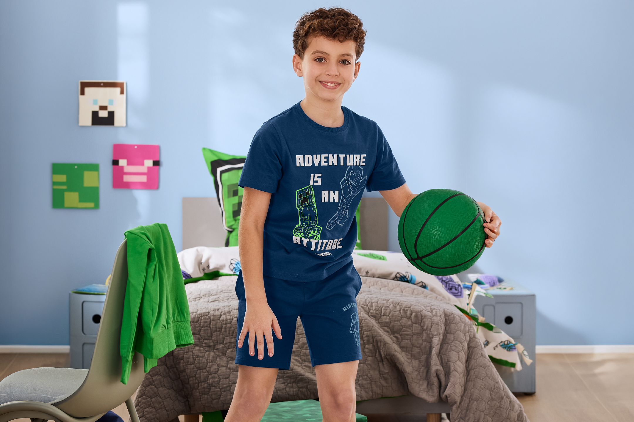 Αγόρι με μπλε μπλουζάκι και σορτς με πράσινη μπάλα μπάσκετ σε δωμάτιο με θέμα Minecraft.