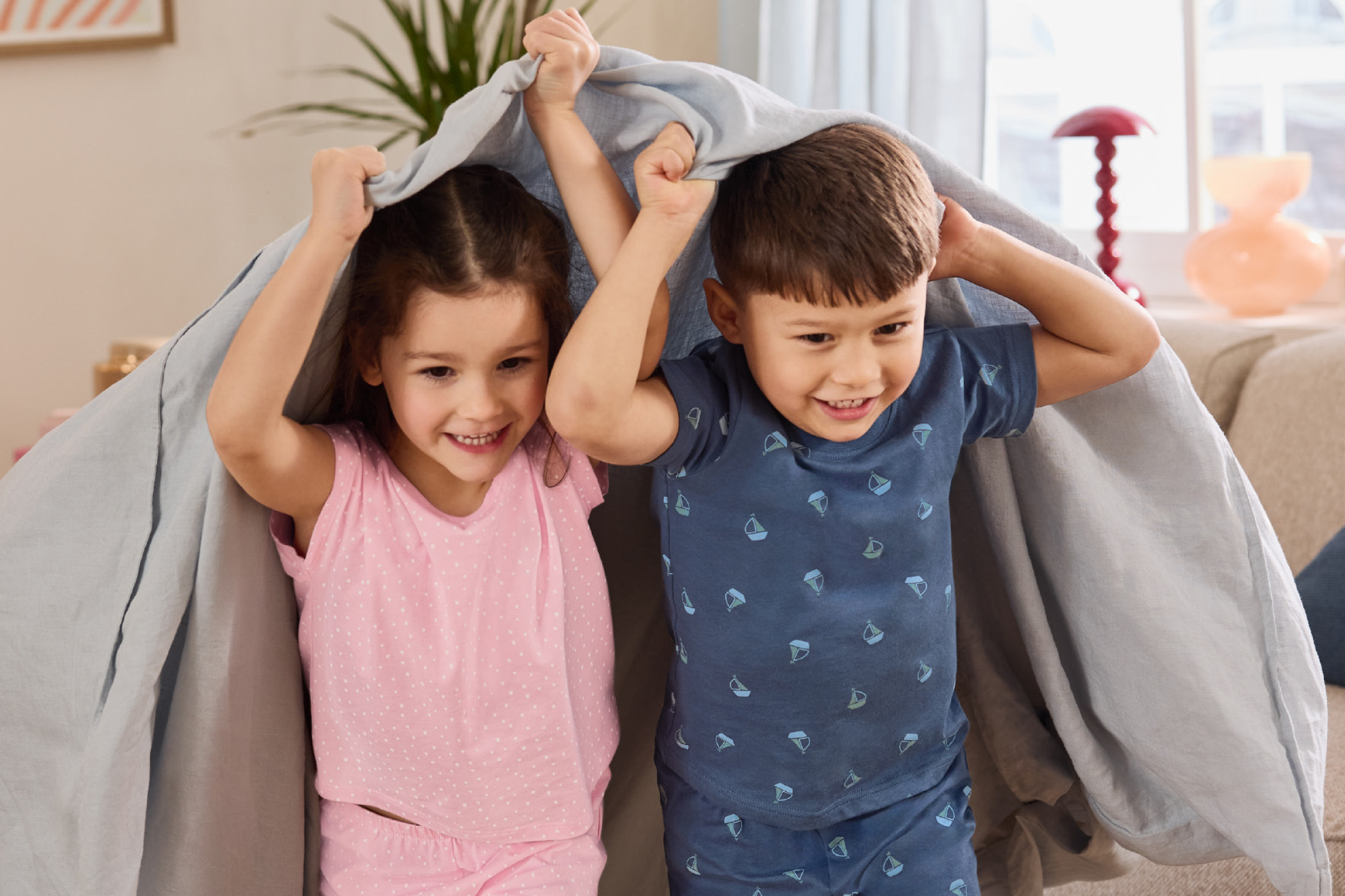 Two children in pajamas playing under a light grey duvet cover.