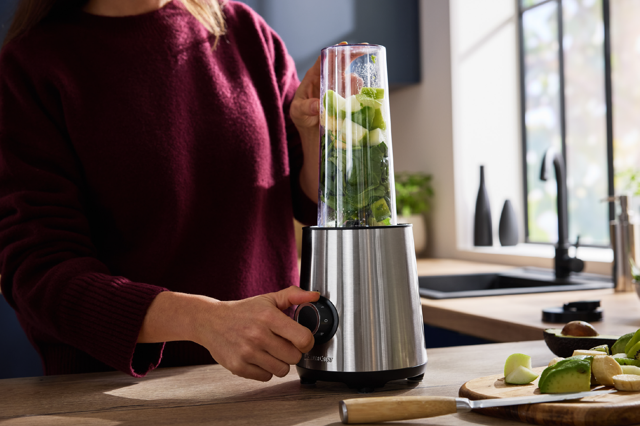 A person preparing a green smoothie with a blender in a modern kitchen.