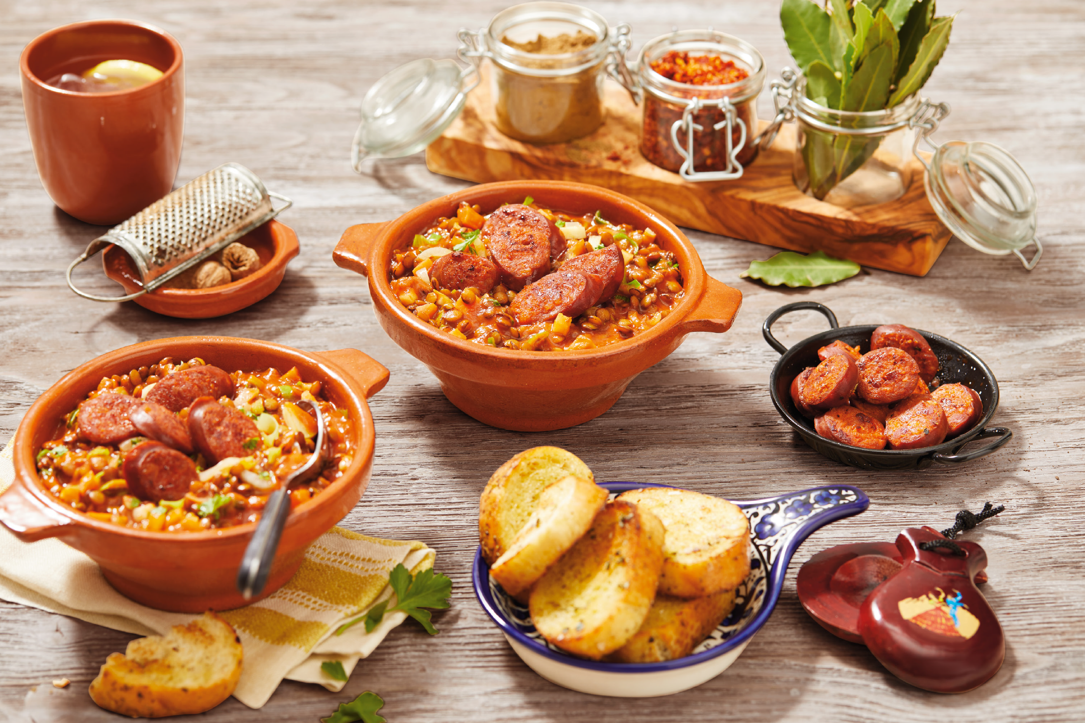 Two terracotta bowls of lentil stew with chorizo, garlic bread, and spices on a wooden table.