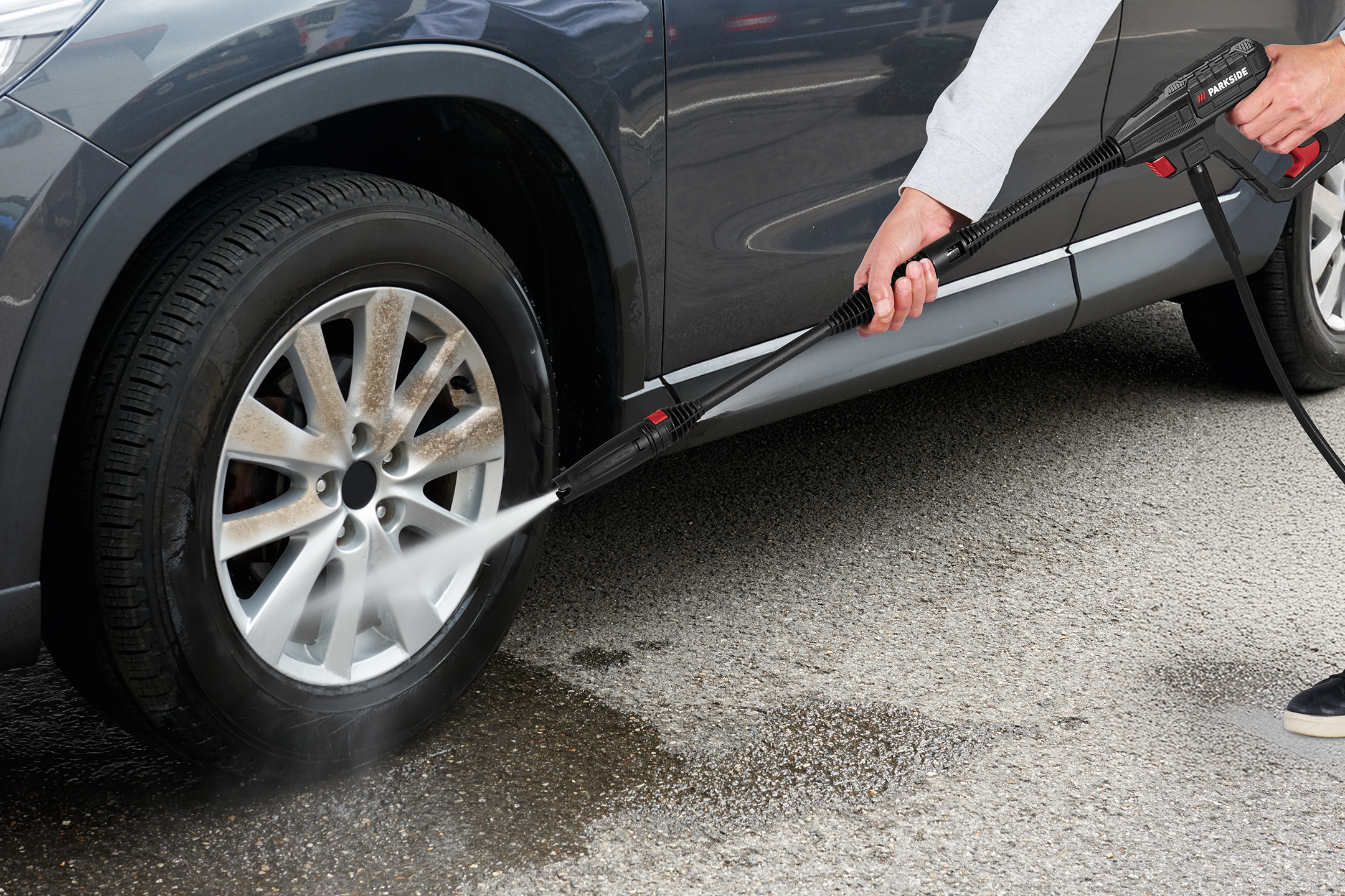 Person cleaning a car wheel with a pressure washer.