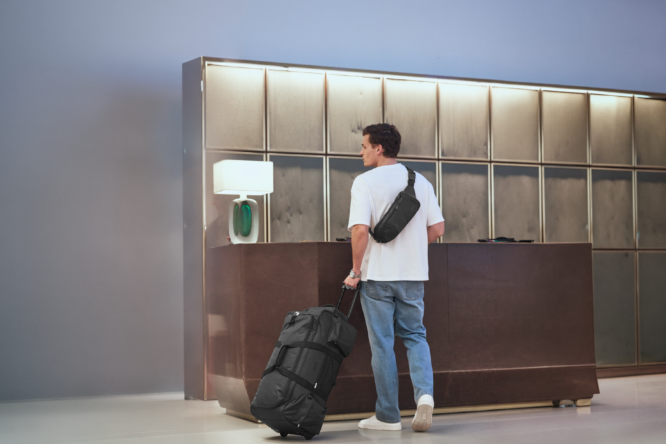 Man with a black duffel bag and a crossbody bag at a hotel reception.