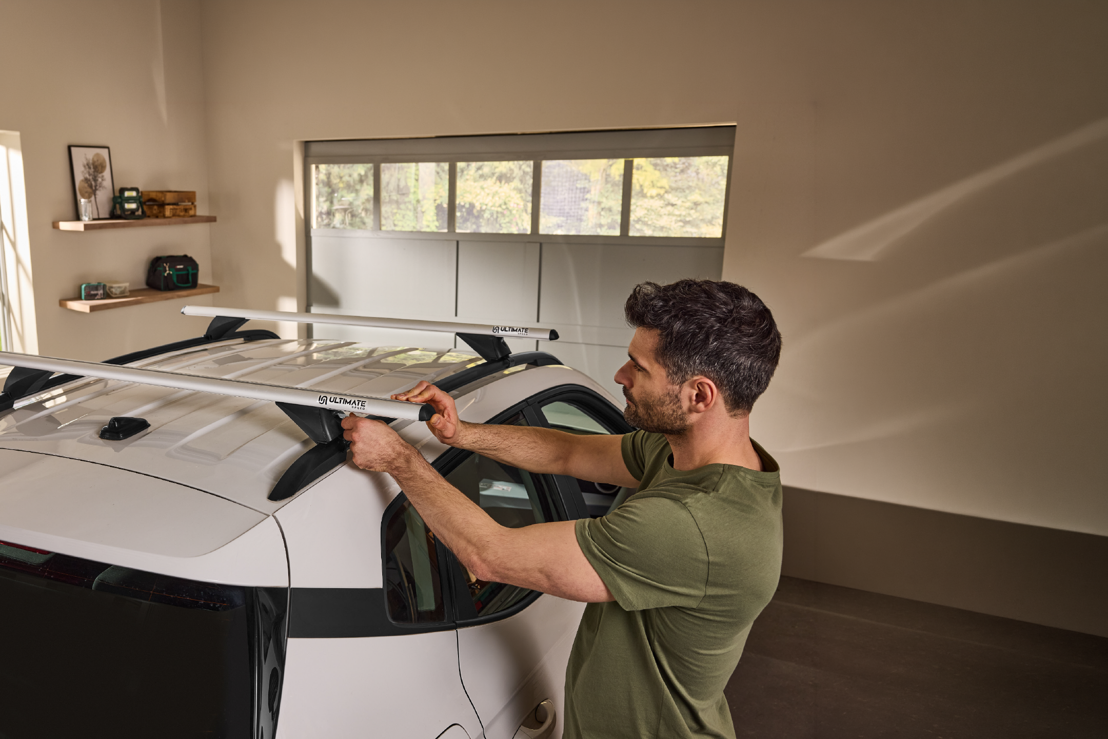 Man installing car roof bars on a white car in a garage.