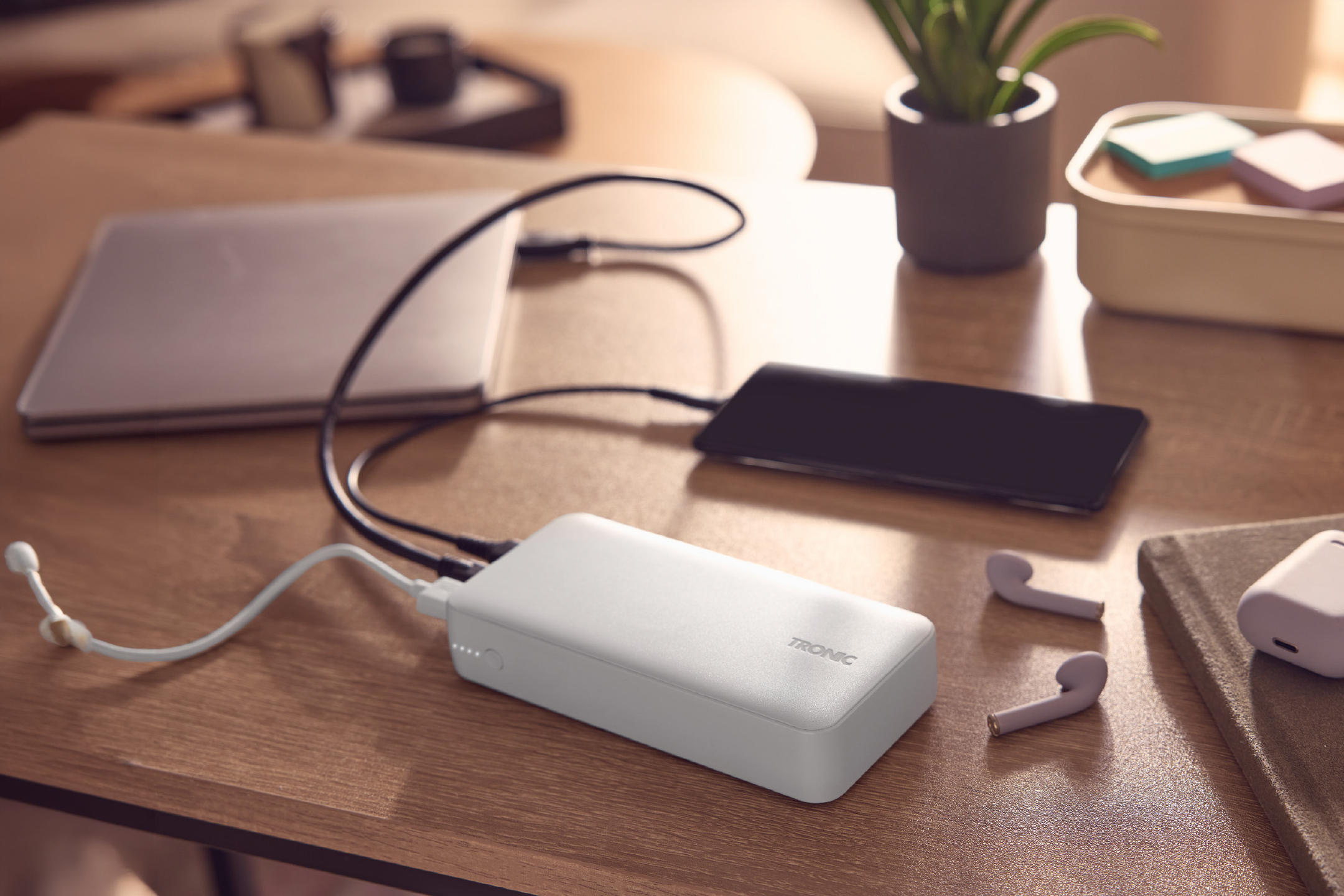 Λευκό power bank φορτίζει φορητό υπολογιστή και smartphone σε ξύλινο γραφείο.