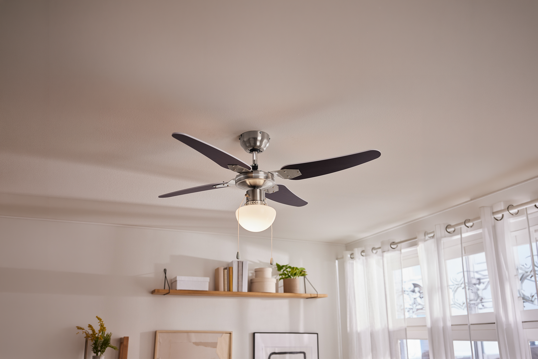 Ceiling fan with light in a living room with a shelf and window curtains.