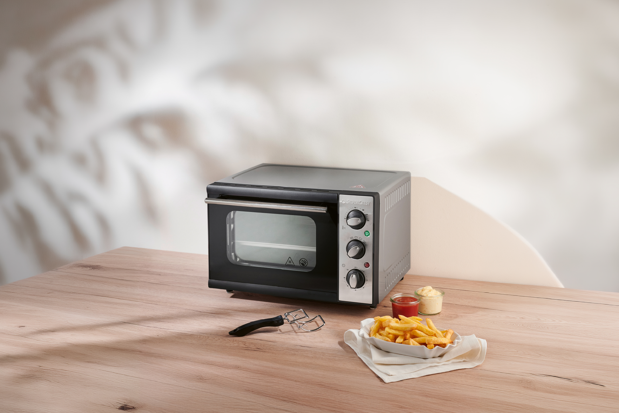 Mini oven with fries, ketchup, and mayonnaise on a wooden table.