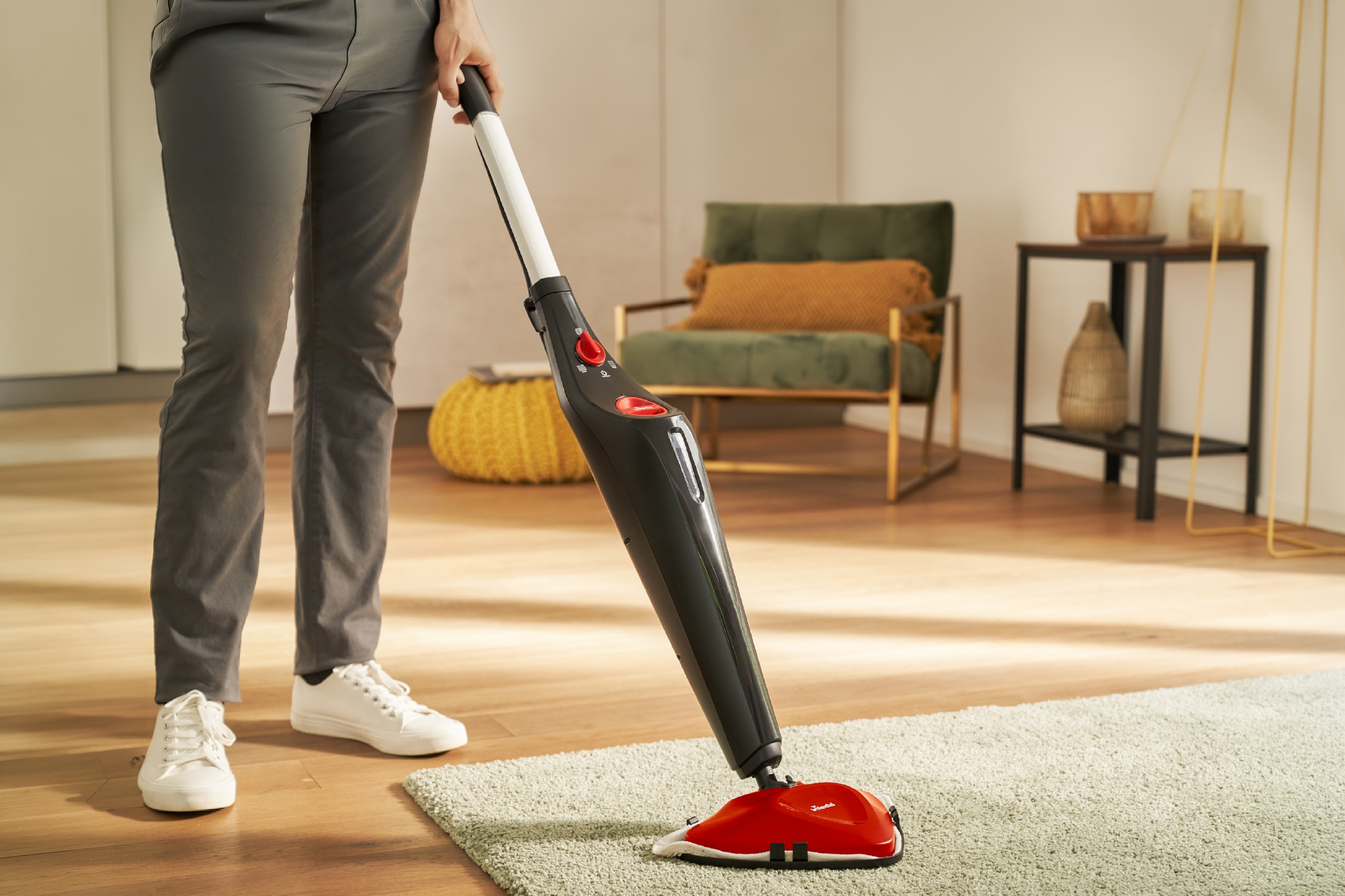 Person cleaning a wooden floor and rug with a steam mop.