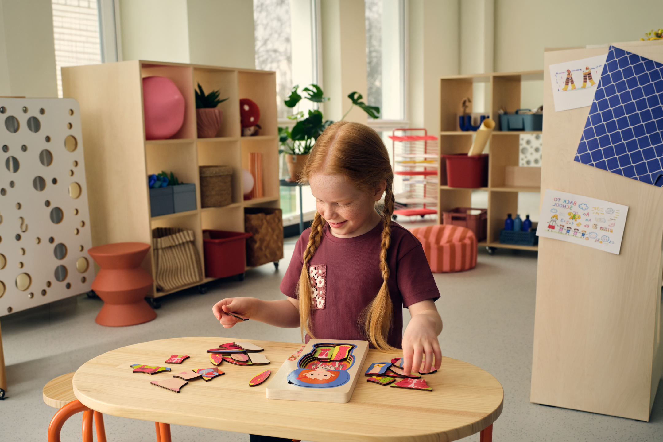 Girl with pigtails playing with a wooden puzzle at a table in a children's room.