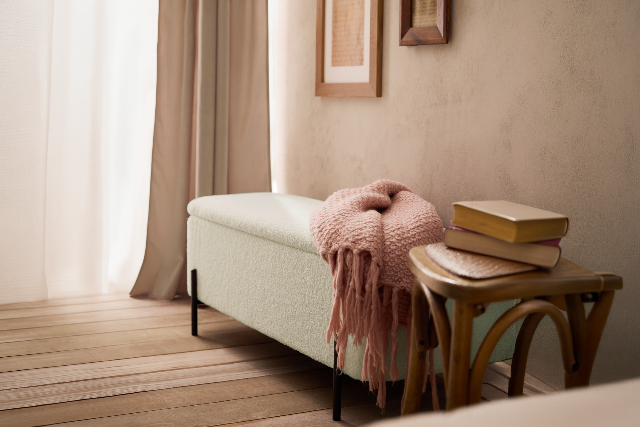 A cozy upholstered storage bench with a pink throw blanket next to a wooden side table.