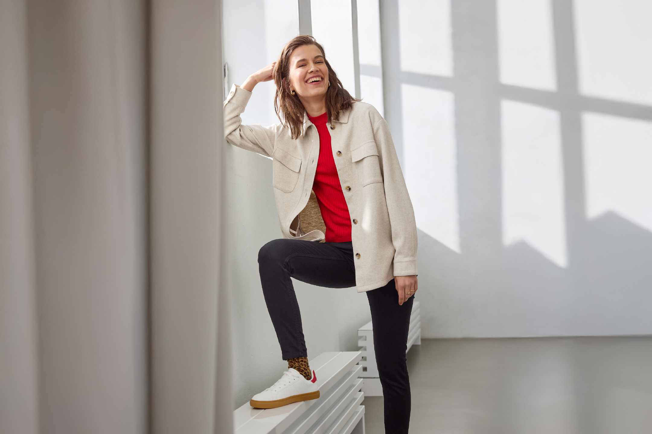Woman in red top, beige jacket, black trousers, and white sneakers with leopard socks