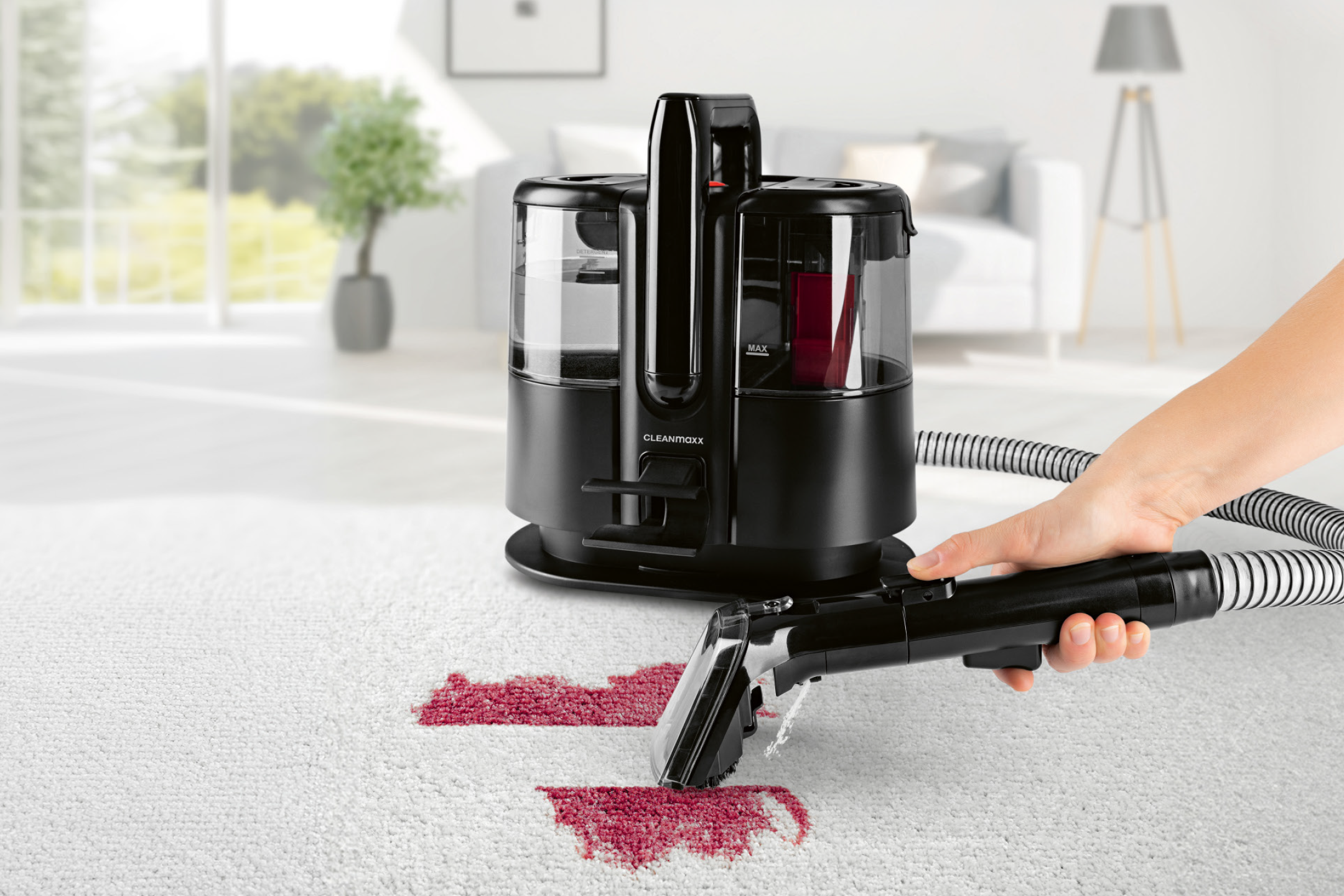 Καθαριστής χαλιών αφαιρεί κόκκινους λεκέδες από λευκό χαλί σε φωτεινό σαλόνι.