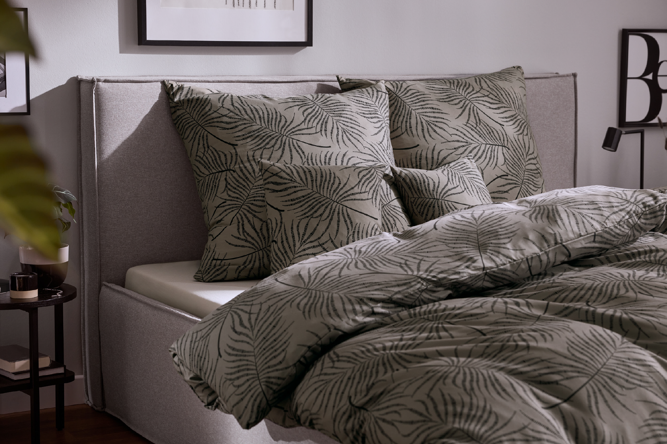 Bedroom with a grey upholstered bed, palm leaf patterned duvet cover and pillows.