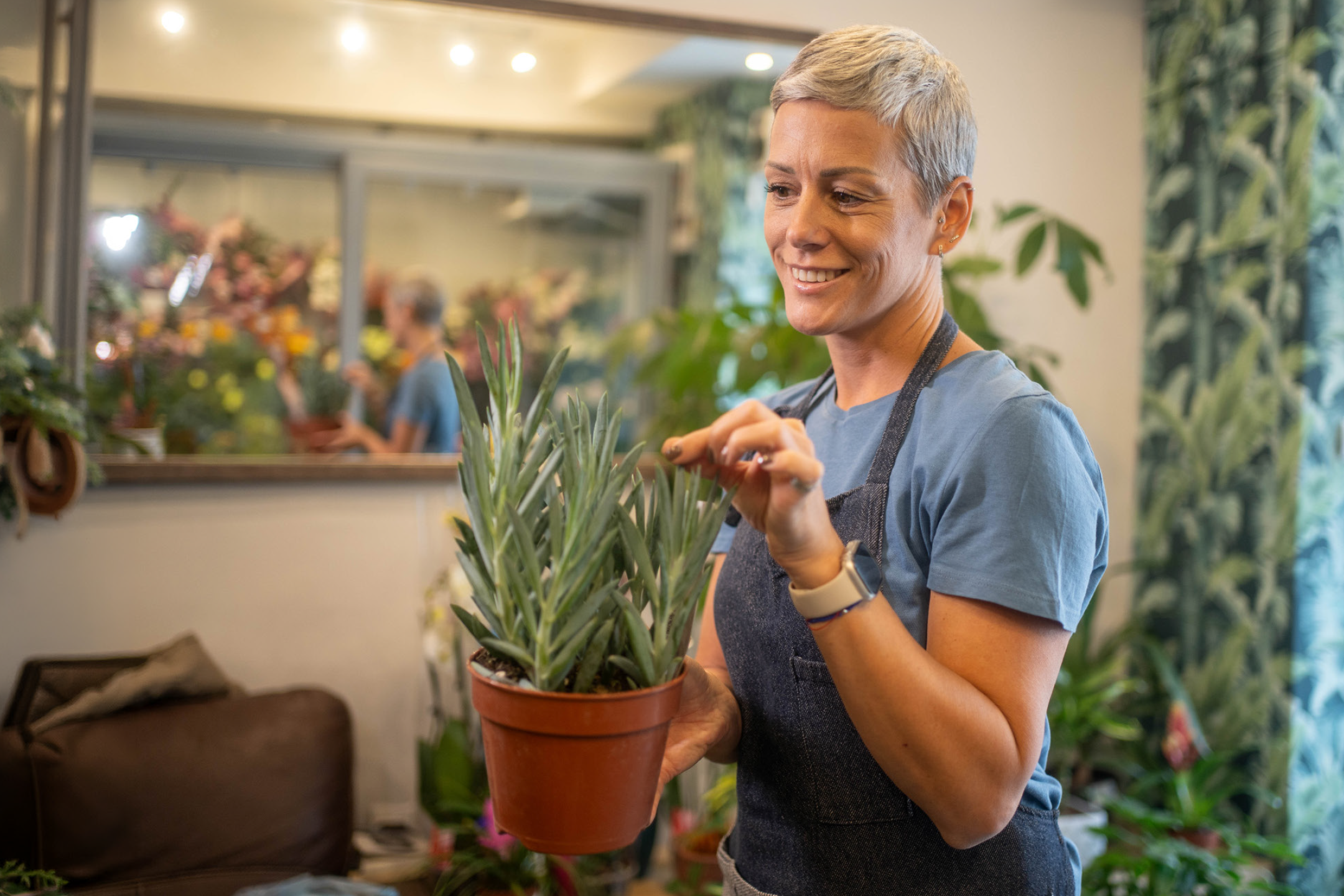 Smiling woman in apron holding a potted succulent plant in a flower shop.