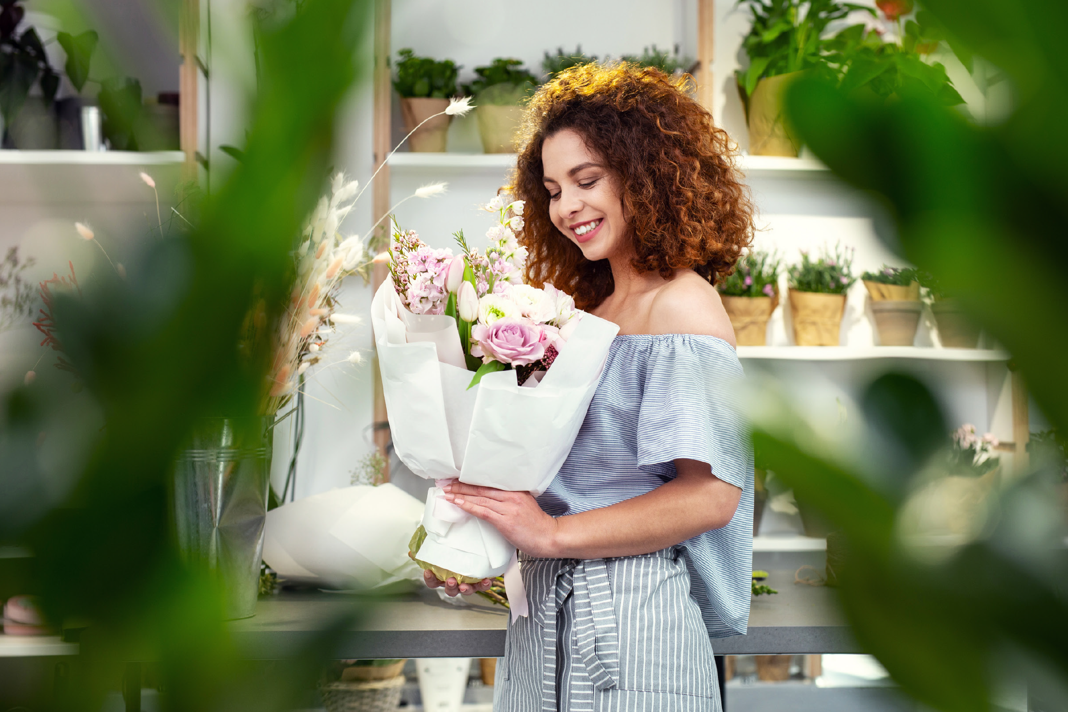 Smiling woman holding a fresh bouquet of pink and white flowers in a flower shop.