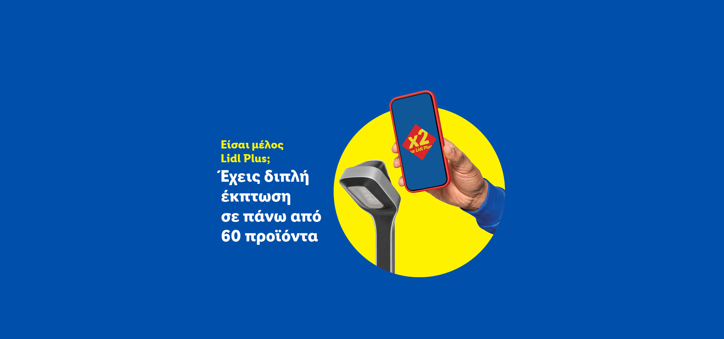 Ένα χέρι κρατάει ένα smartphone με το λογότυπο 'x2 με Lidl Plus', δίπλα σε ένα φωτιστικό δρόμου.