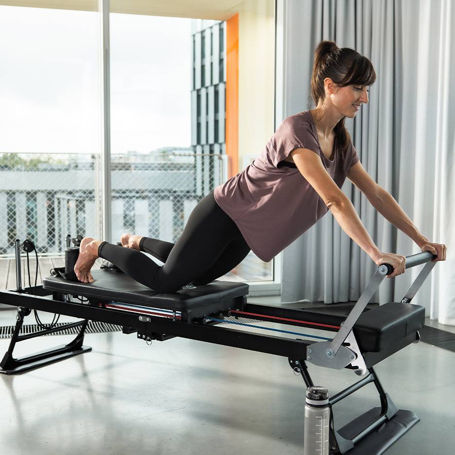 Woman exercising Pilates on a reformer with springs and straps.