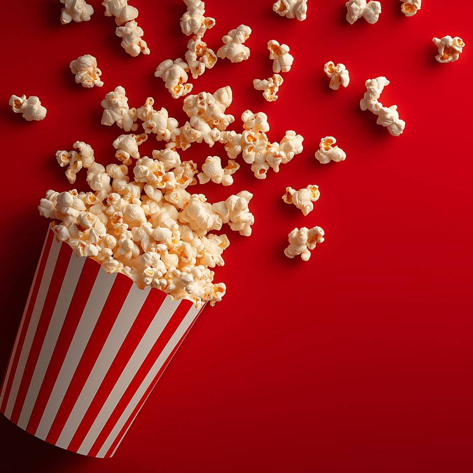 Popcorn on a red background, some of the popcorn in a striped cardboard container.