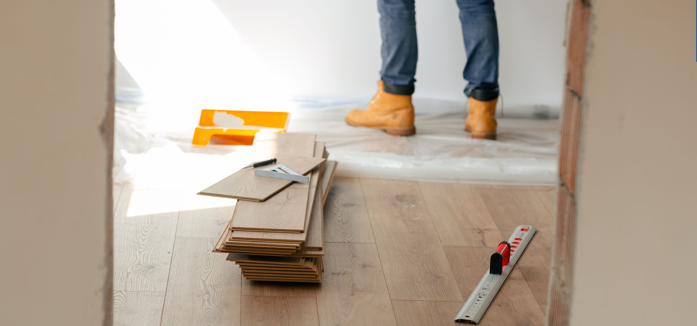 Σανίδες laminate δαπέδου και εργαλεία εγκατάστασης σε ξύλινο πάτωμα, με ένα άτομο με μπότες.